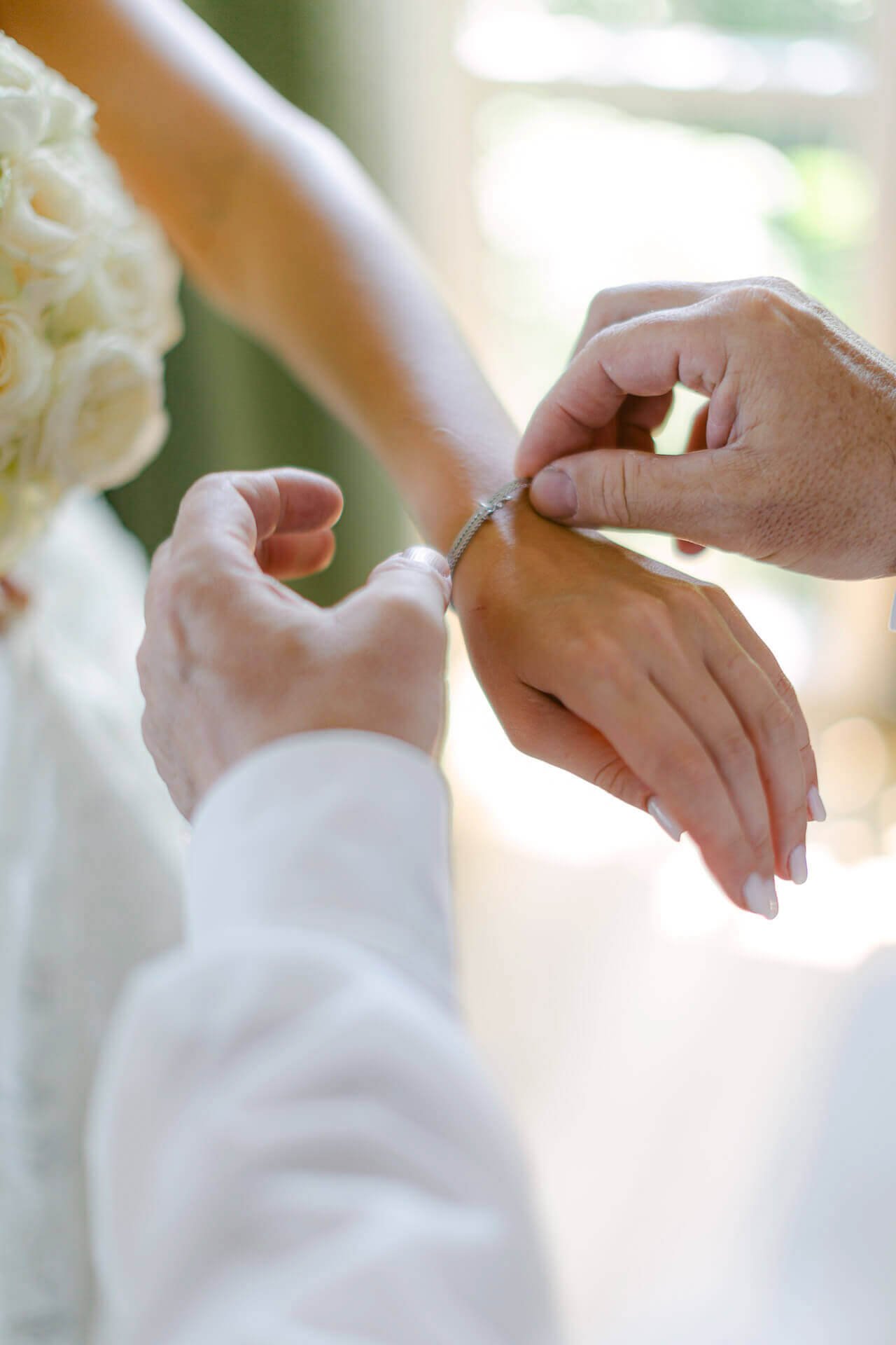 Nahaufnahme einer Person, die einem anderen eine silberne Armbanduhr anlegt. Der Hintergrund ist verschwommen und zeigt weiche, natürliche Beleuchtung.