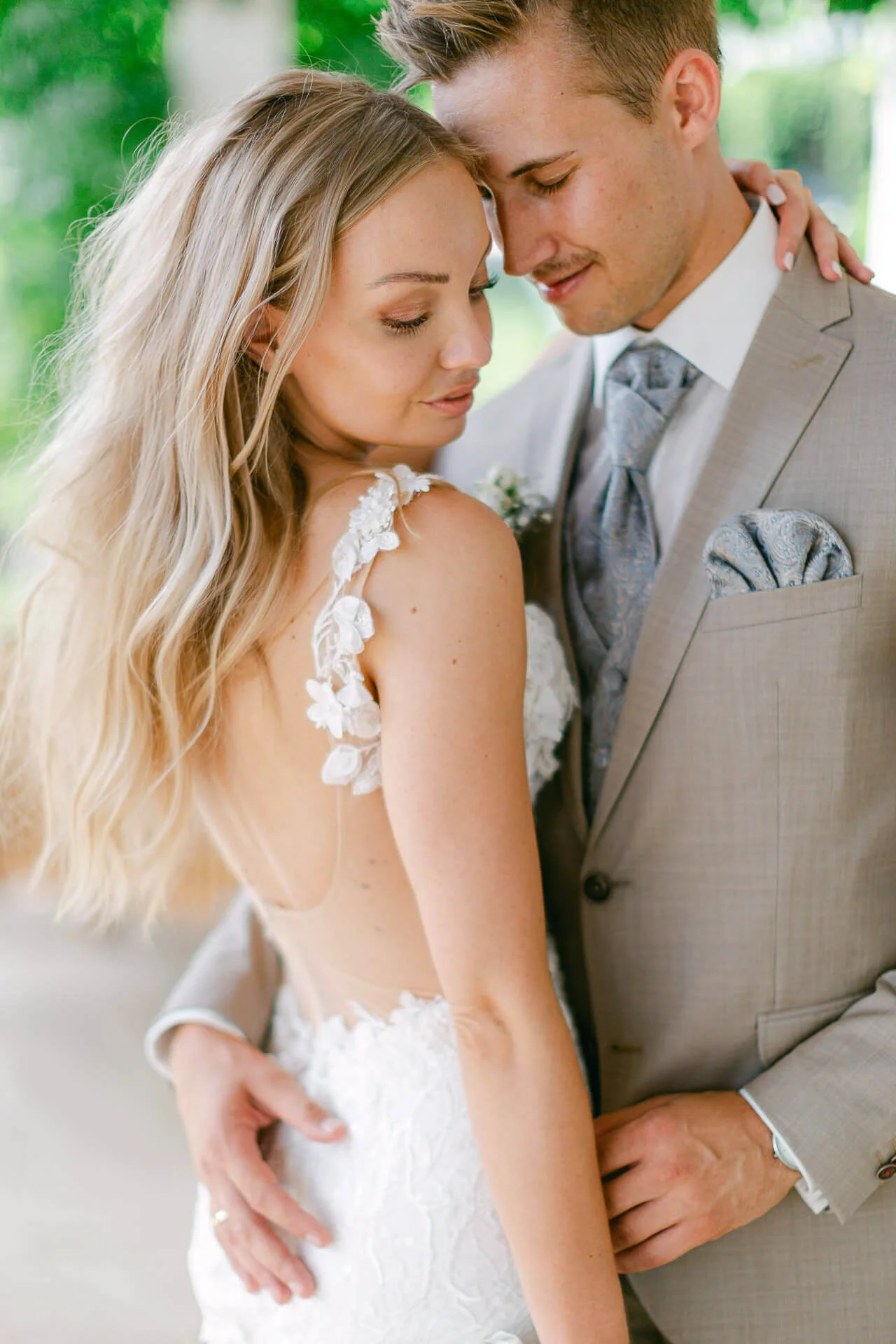 Ein Brautpaar in eleganter Hochzeitskleidung, eng umschlungen in einem romantischen Moment. Die Braut trägt ein weißes Spitzenkleid, der Bräutigam einen hellen Anzug.