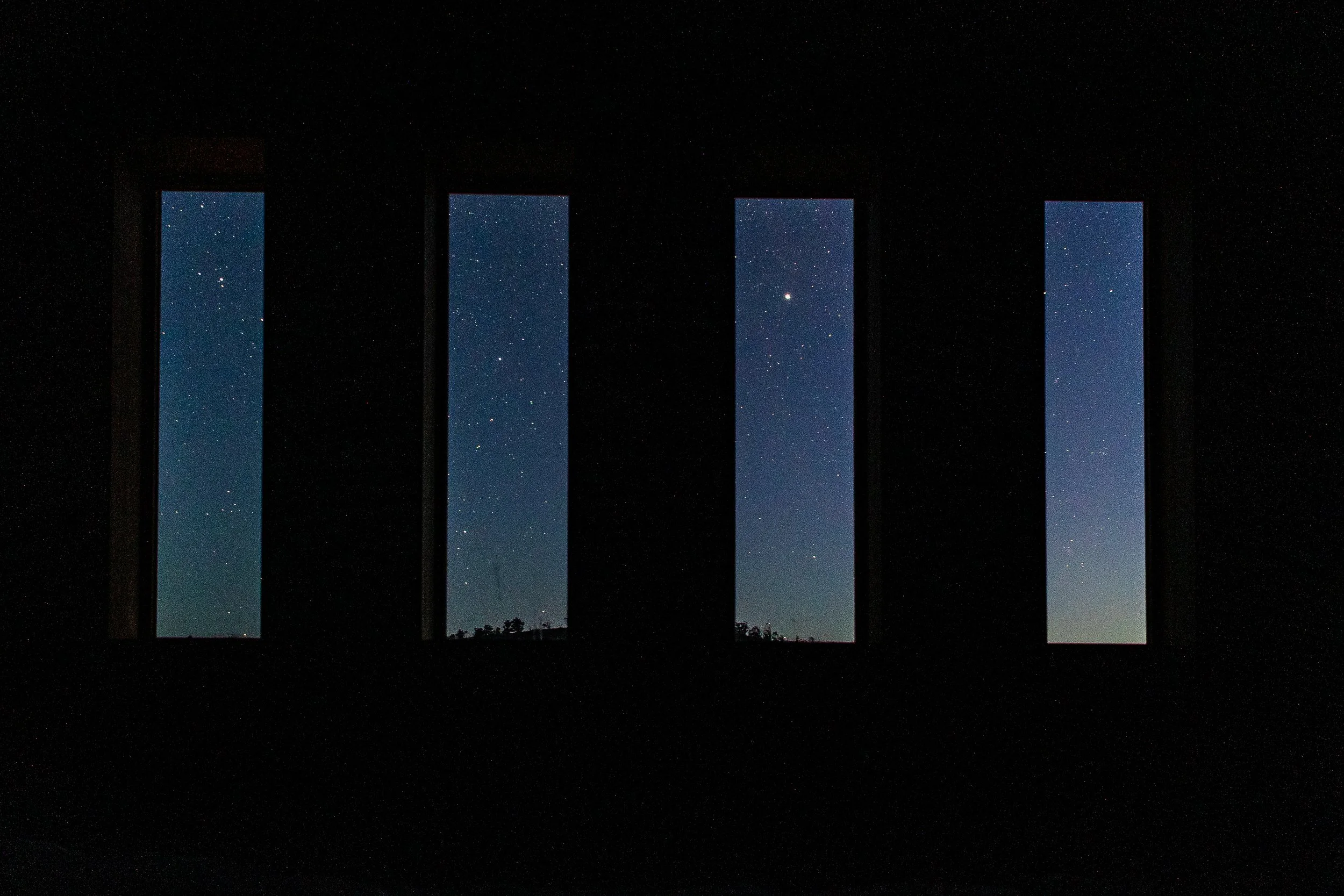 View of a starry night sky through four tall, narrow windows.