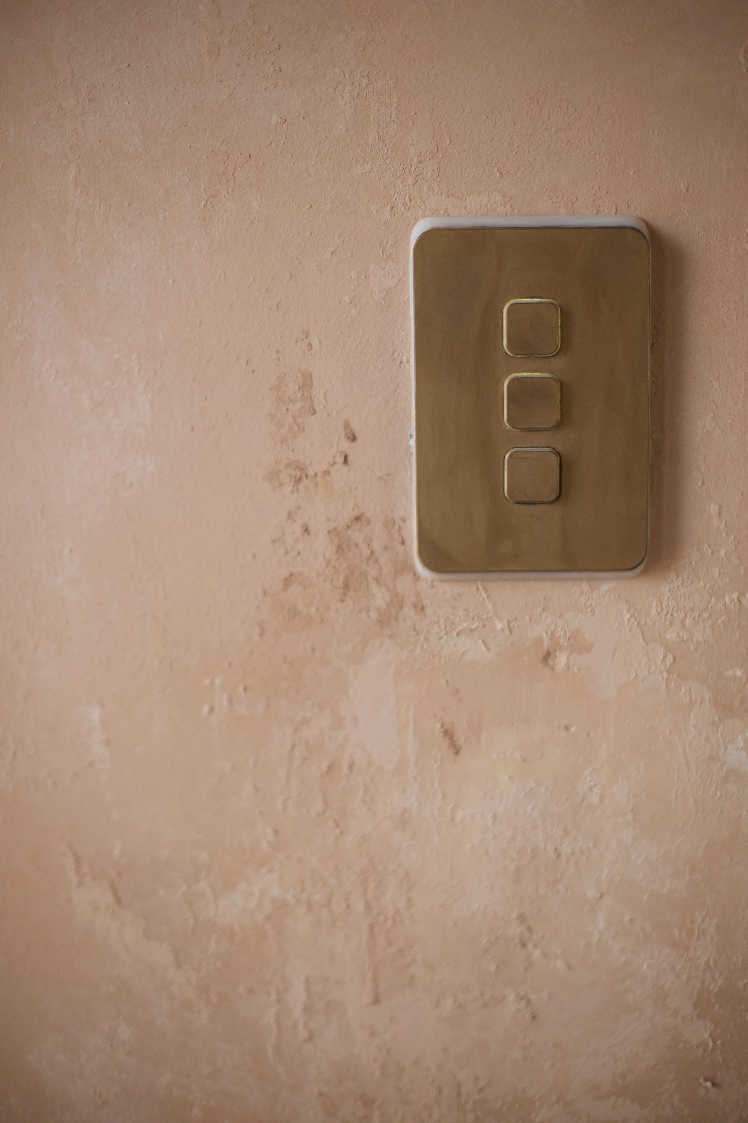 A beige-colored wall with a textured finish and a beige switch plate with three square, metallic toggles.