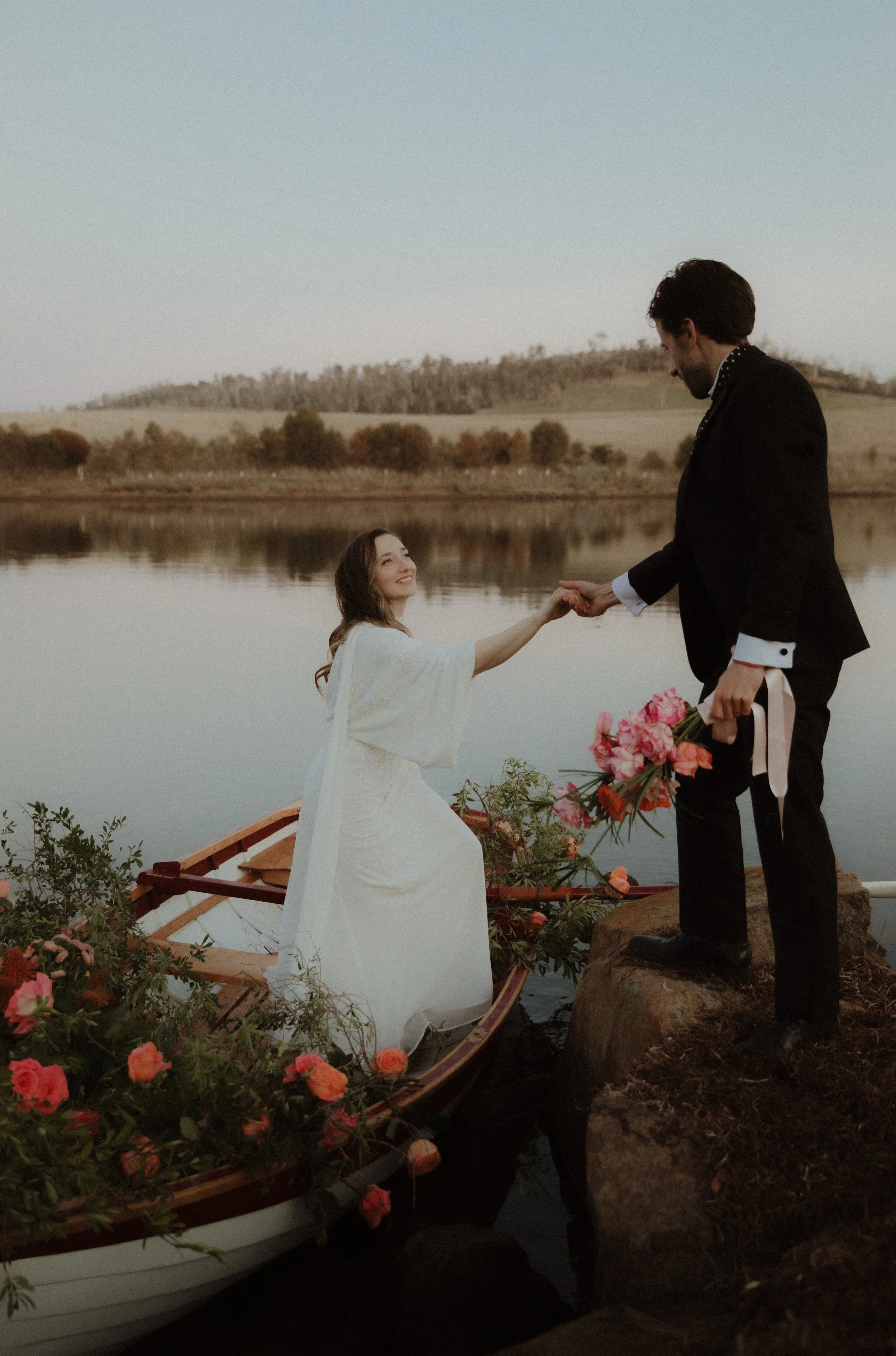 Bride and groom disembarking romantic rowboat on the river.  The boat is filled with flowers.