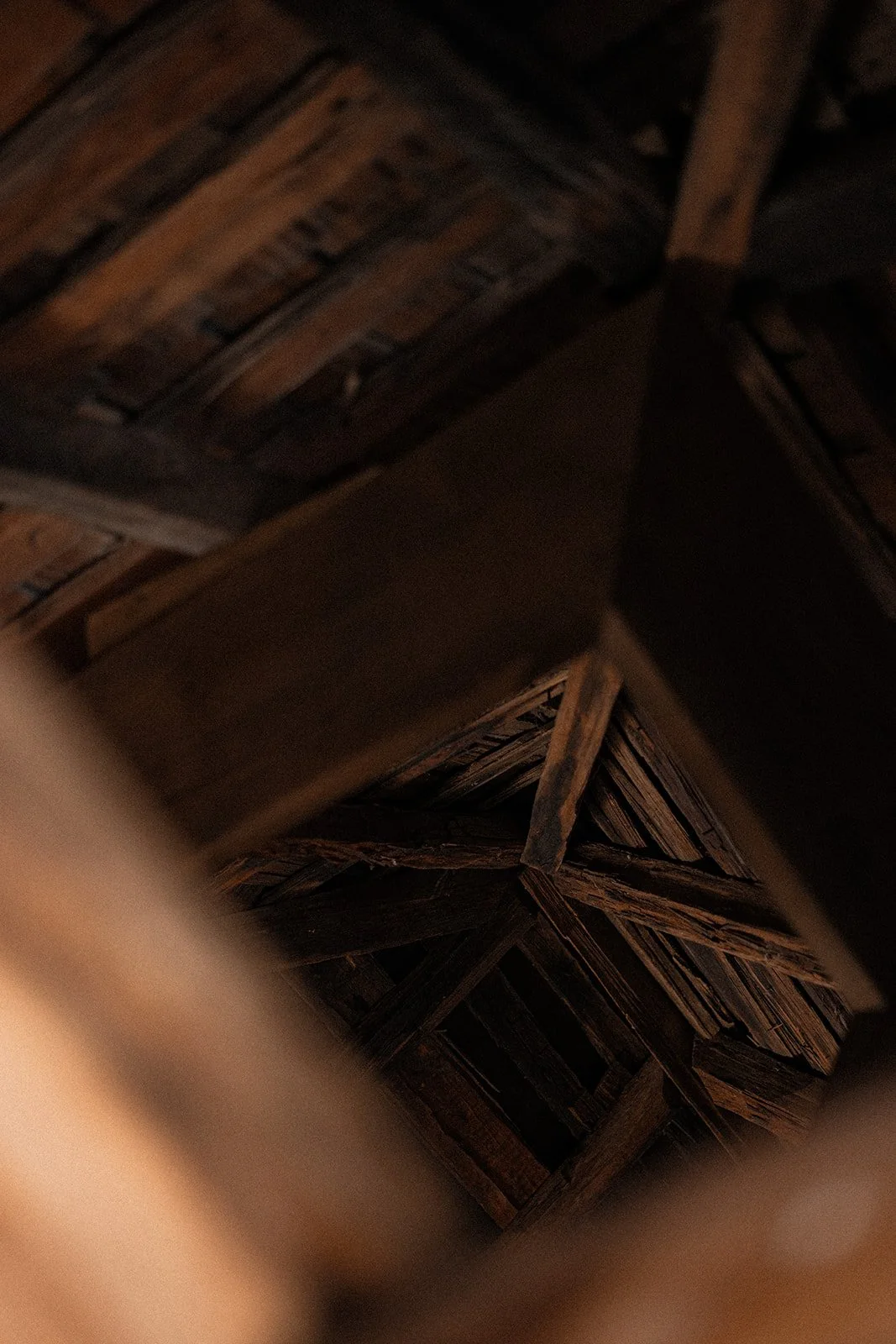 Looking up inside a wooden attic or storage space, showing wooden beams and planks, with some parts blurred in the foreground.
