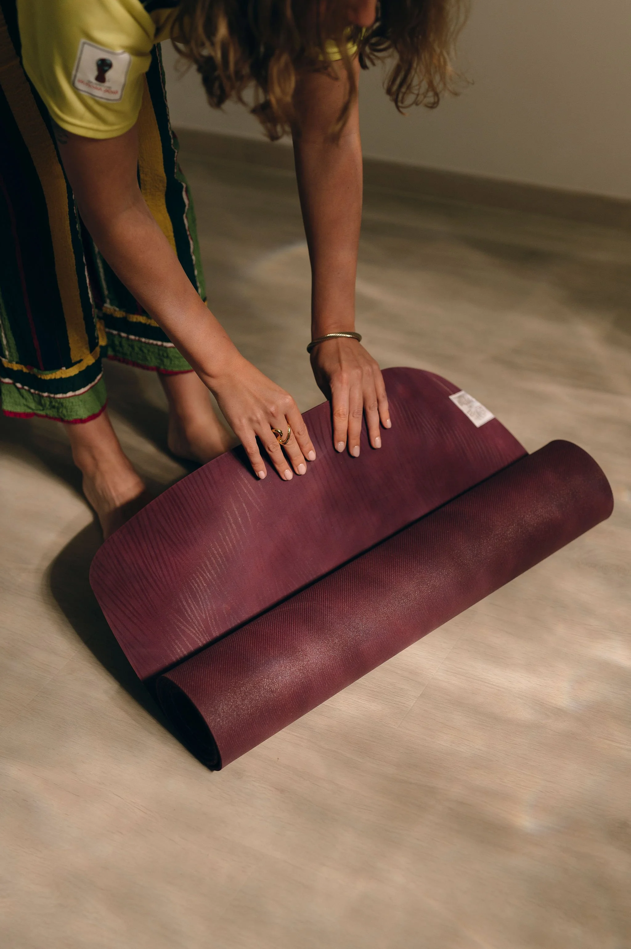 Une personne plie un tapis de yoga de couleur bordeaux sur un sol en bois clair.
