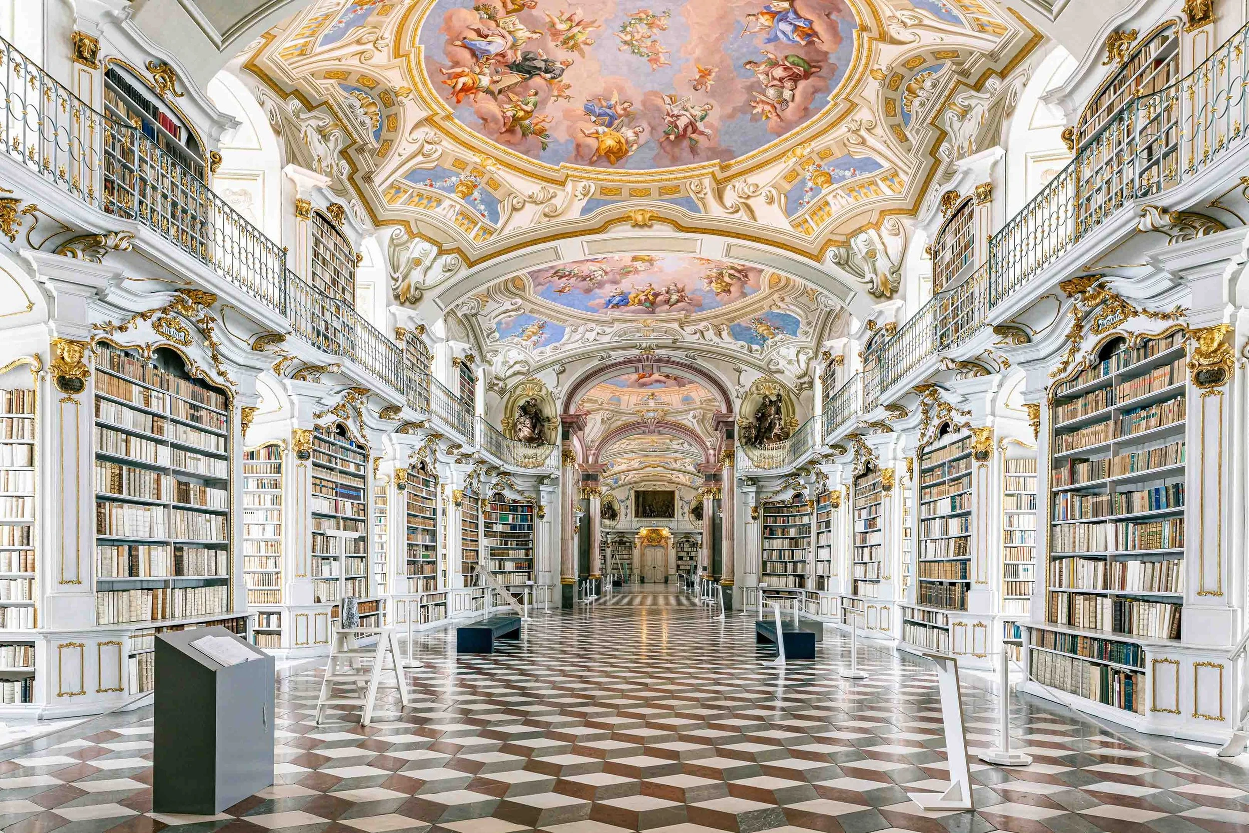 Prunkvolle Bibliothek im Stift Admont mit verzierten Regalen, barockem Deckenfresko und geometrischem Bodenmuster.