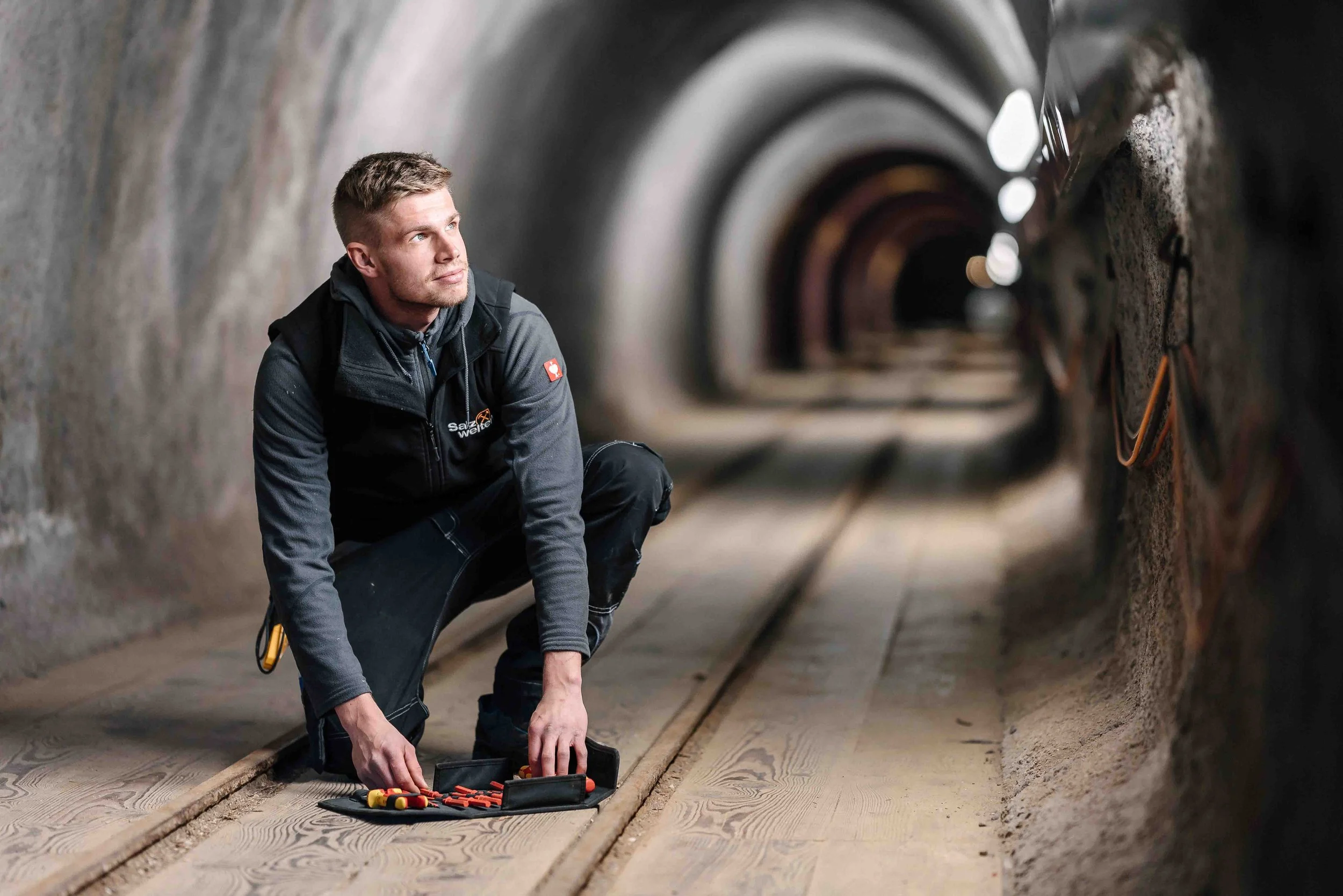 Ein Mann in einer Tunnelumgebung, der auf dem Boden kniet und mit Werkzeug hantiert.