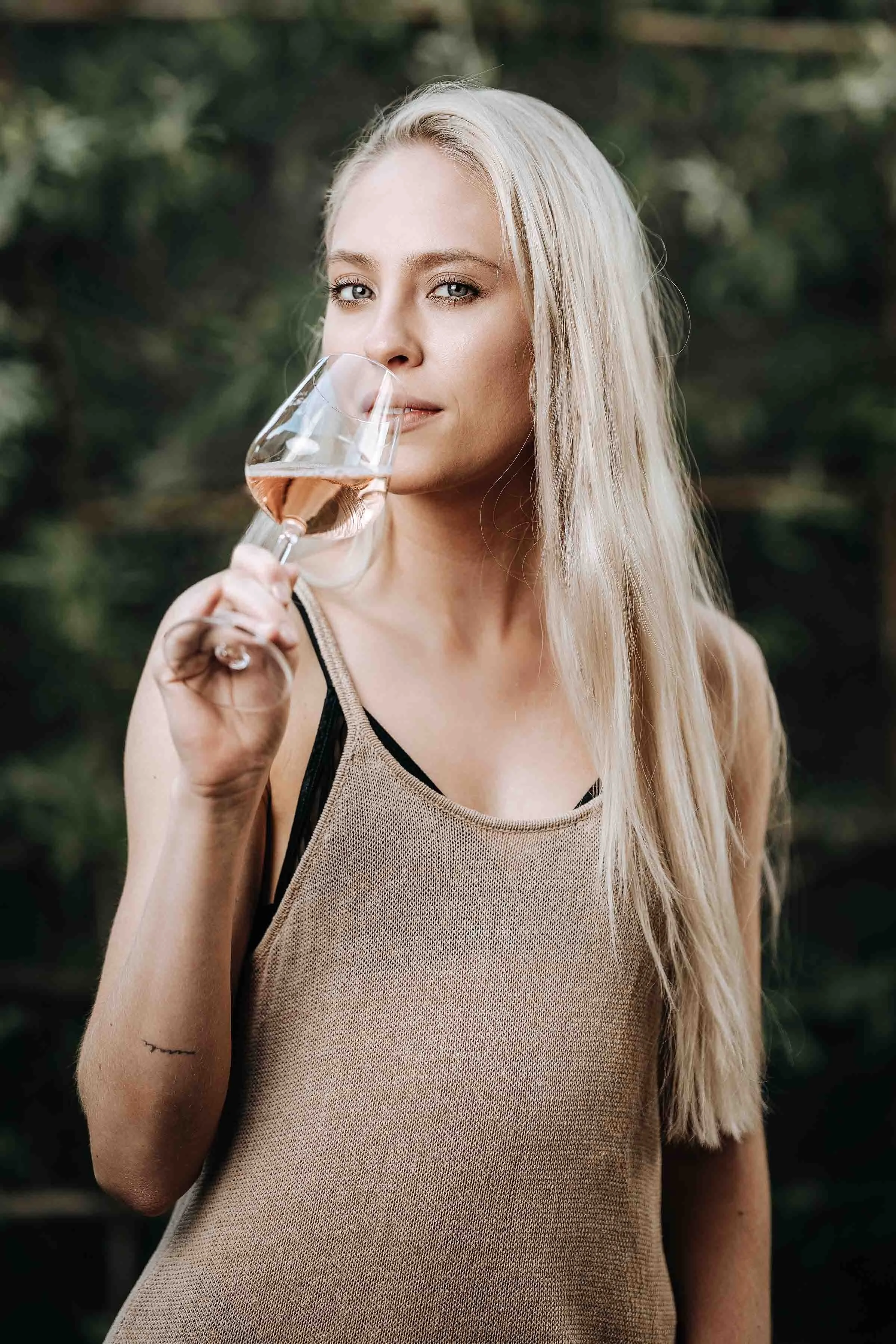 Frau riecht an einem Weinglas mit Roséwein in einem Garten.