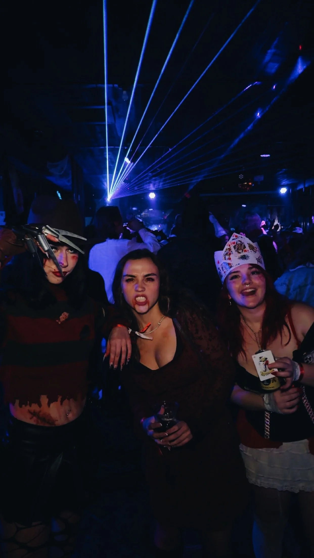 Three women at a nightclub dancing and partying under blue laser lights.