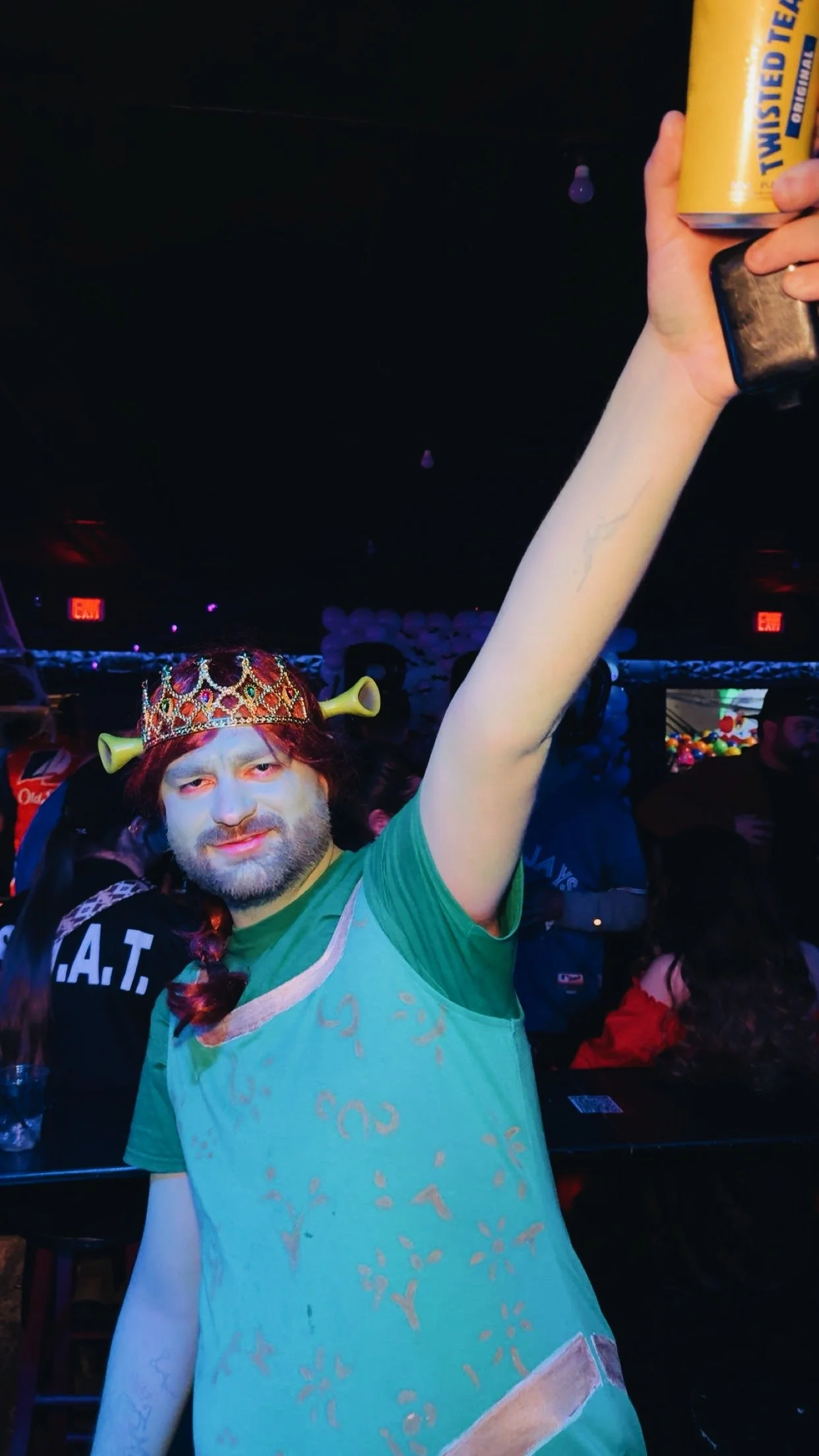 Person dressed as a wizard with a crown and a long beard, holding a yellow can and raising their arm at a party or event.