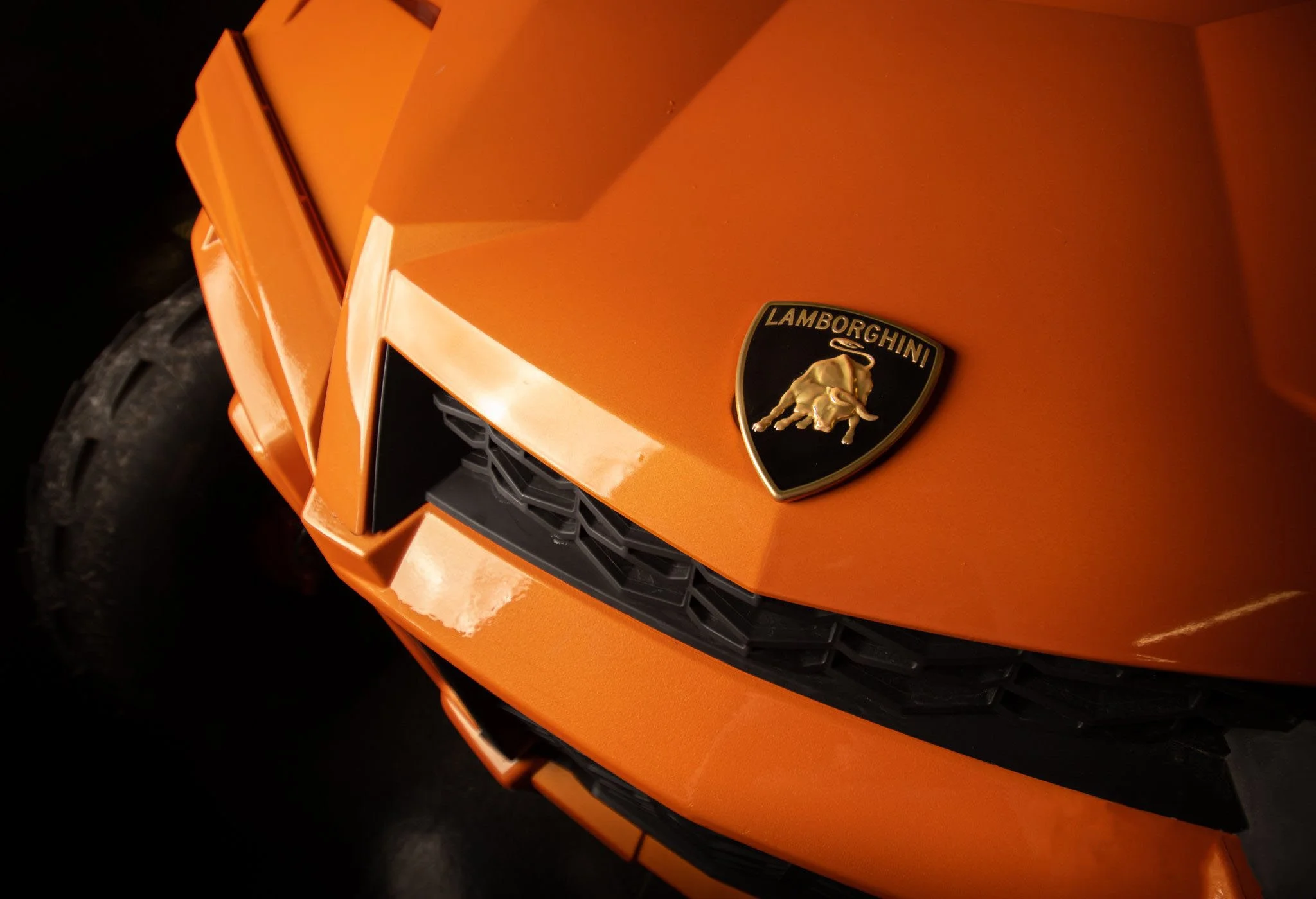 Close-up of an orange Lamborghini with a black grille and a gold and black Lamborghini emblem on the hood.