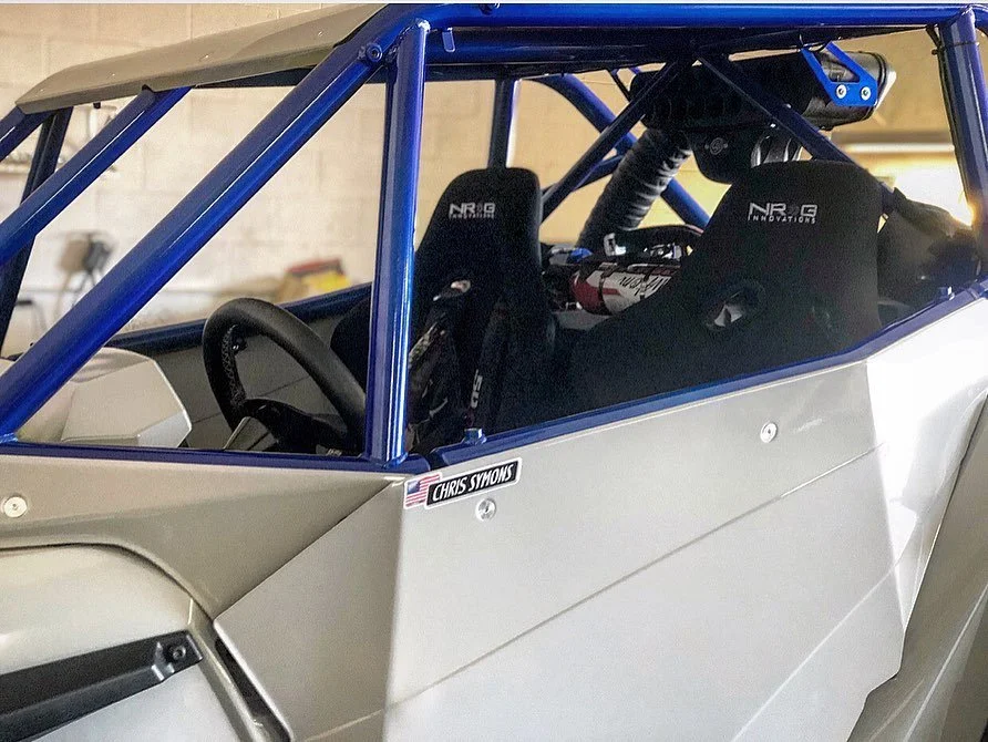 Inside a race car with racing seats and harnesses, blue roll cage, and a driver side LED light.