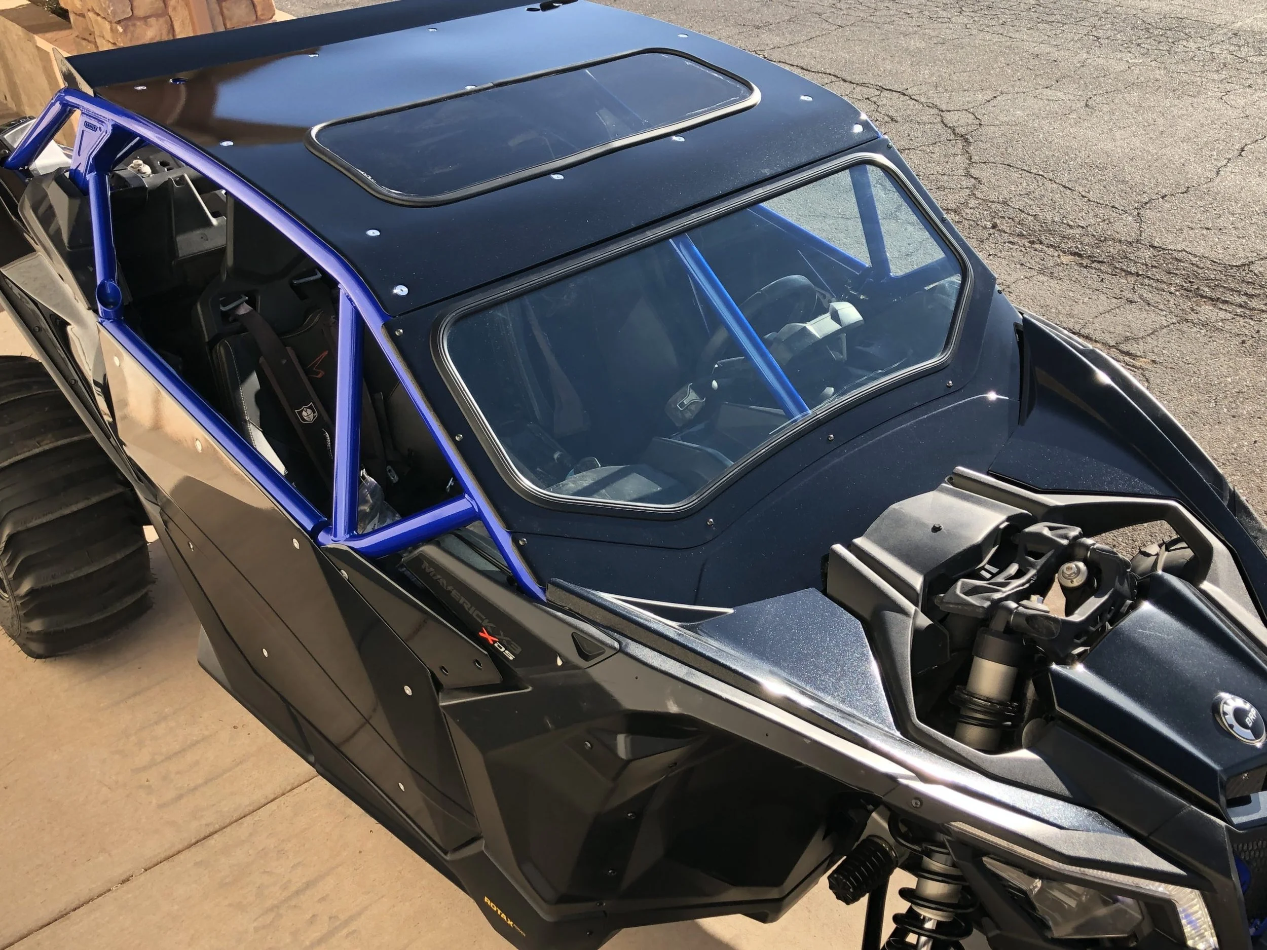 Off-road Polaris RZR side-by-side vehicle with open canopy, blue metal frame, and large rugged tires on pavement.