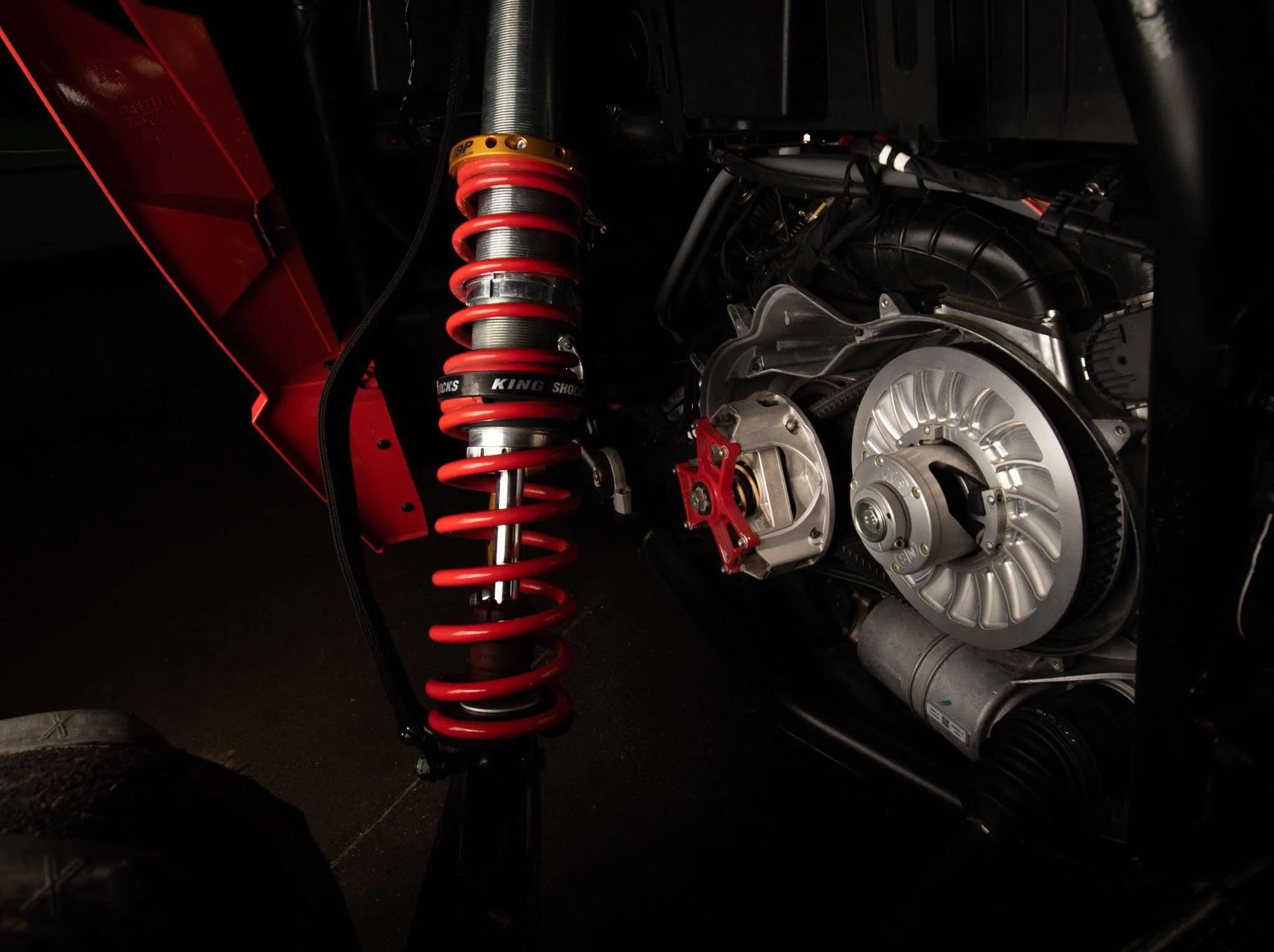 Close-up of a car's suspension and engine parts, with a prominent red coil spring and various mechanical components visible.