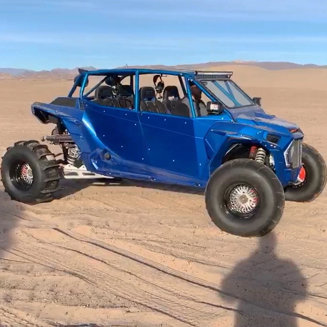 A blue off-road dune buggy in mid-air in a desert landscape under a clear blue sky.