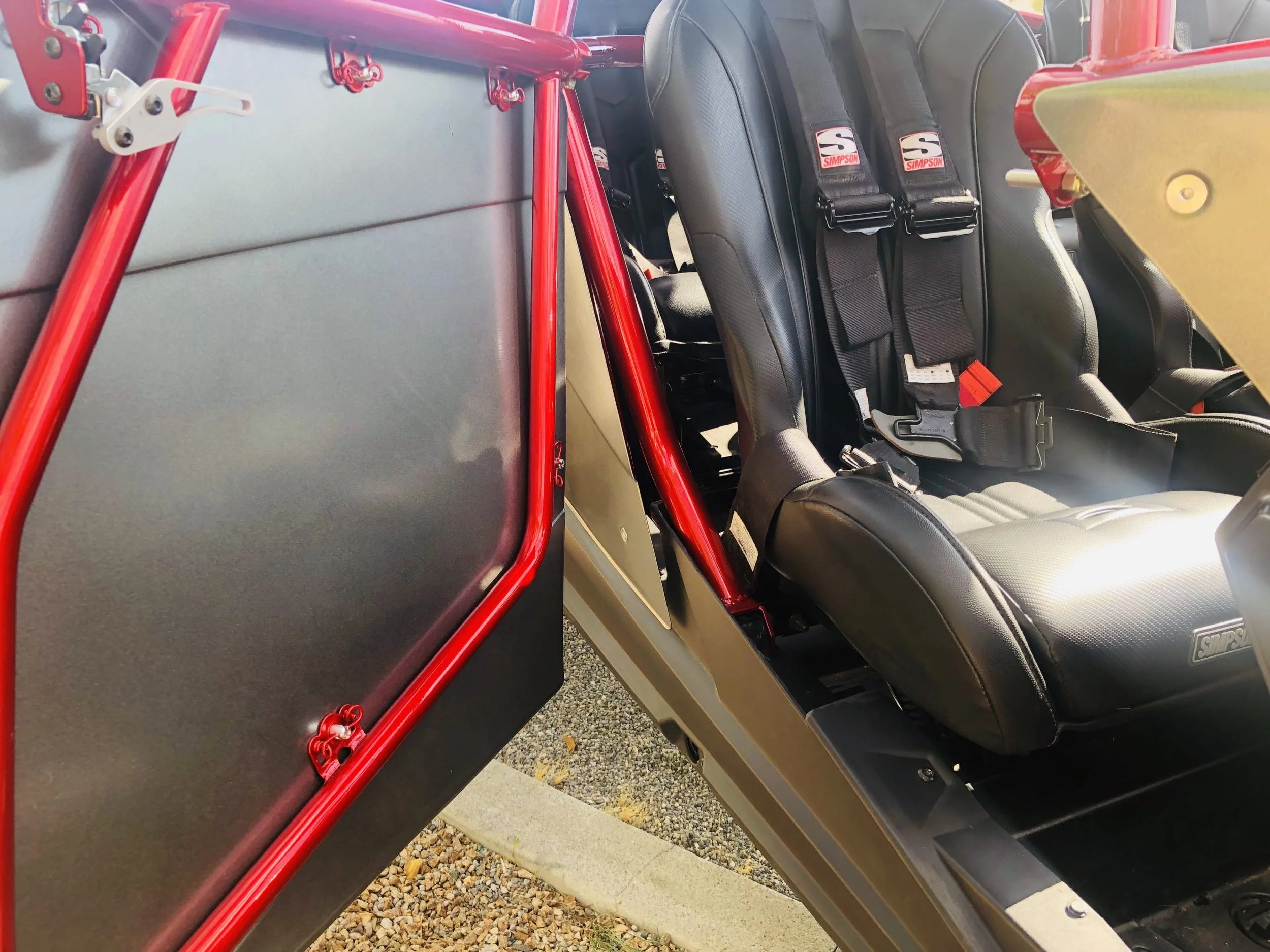 Close-up of race car seats with safety harnesses, visible red roll cage, and a window net on the side of a race car interior.