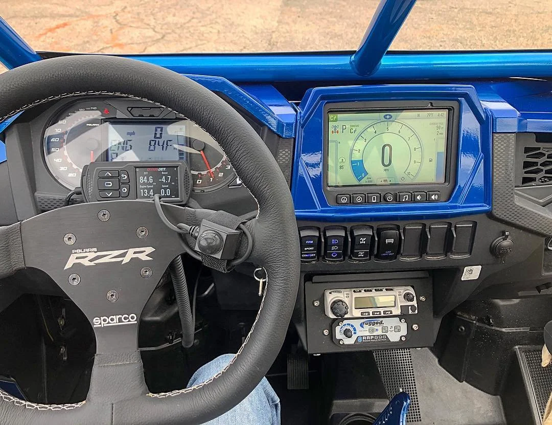 Racing vehicle's dashboard with digital instrument cluster, steering wheel, switch panel, and communication radio.