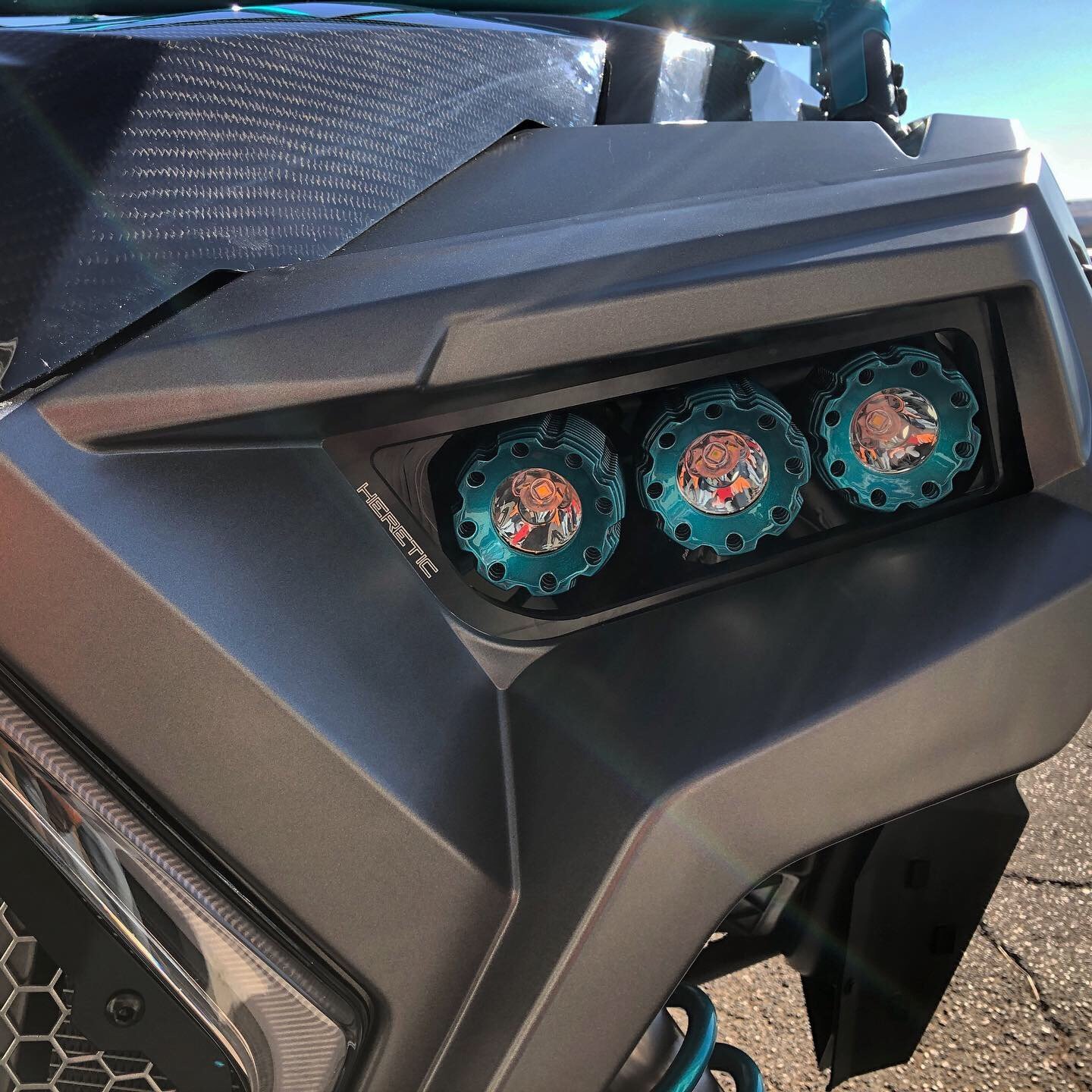 Close-up of a futuristic vehicle headlight assembly with three round LED lights enclosed in blue gear-shaped casings.