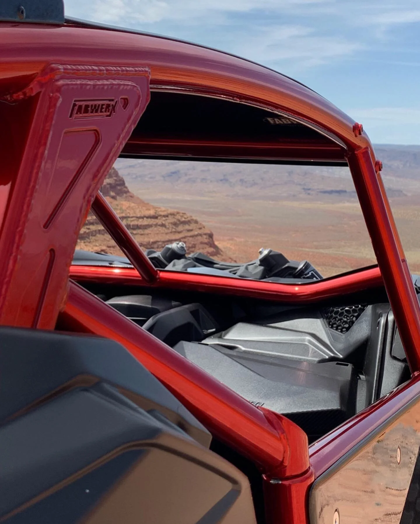 Close-up of a red off-road vehicle with a view of a desert canyon landscape in the background.