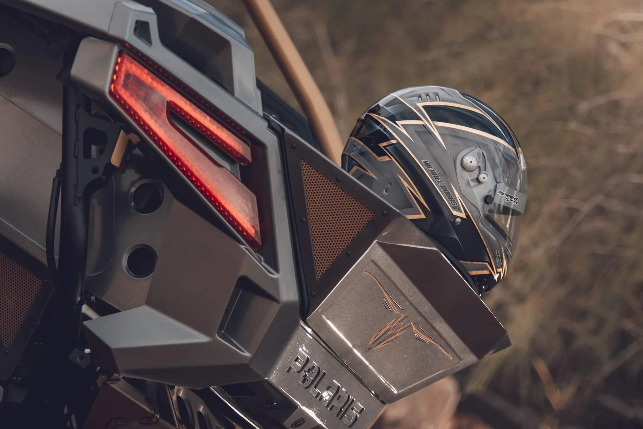 Close-up of a motorcycle's rear with a helmet placed on the luggage rack, featuring red tail lights and a metallic badge reading 'Polaris'.