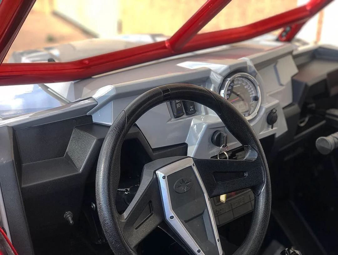 Close-up of a vehicle dashboard and steering wheel, featuring a large speedometer gauge and black plastic interior.