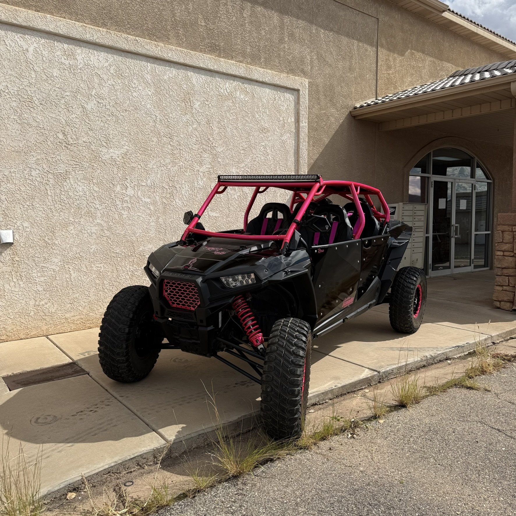 An off-road racing vehicle in a desert landscape, equipped with large tires, a roll cage, and a view of its suspension and engine.