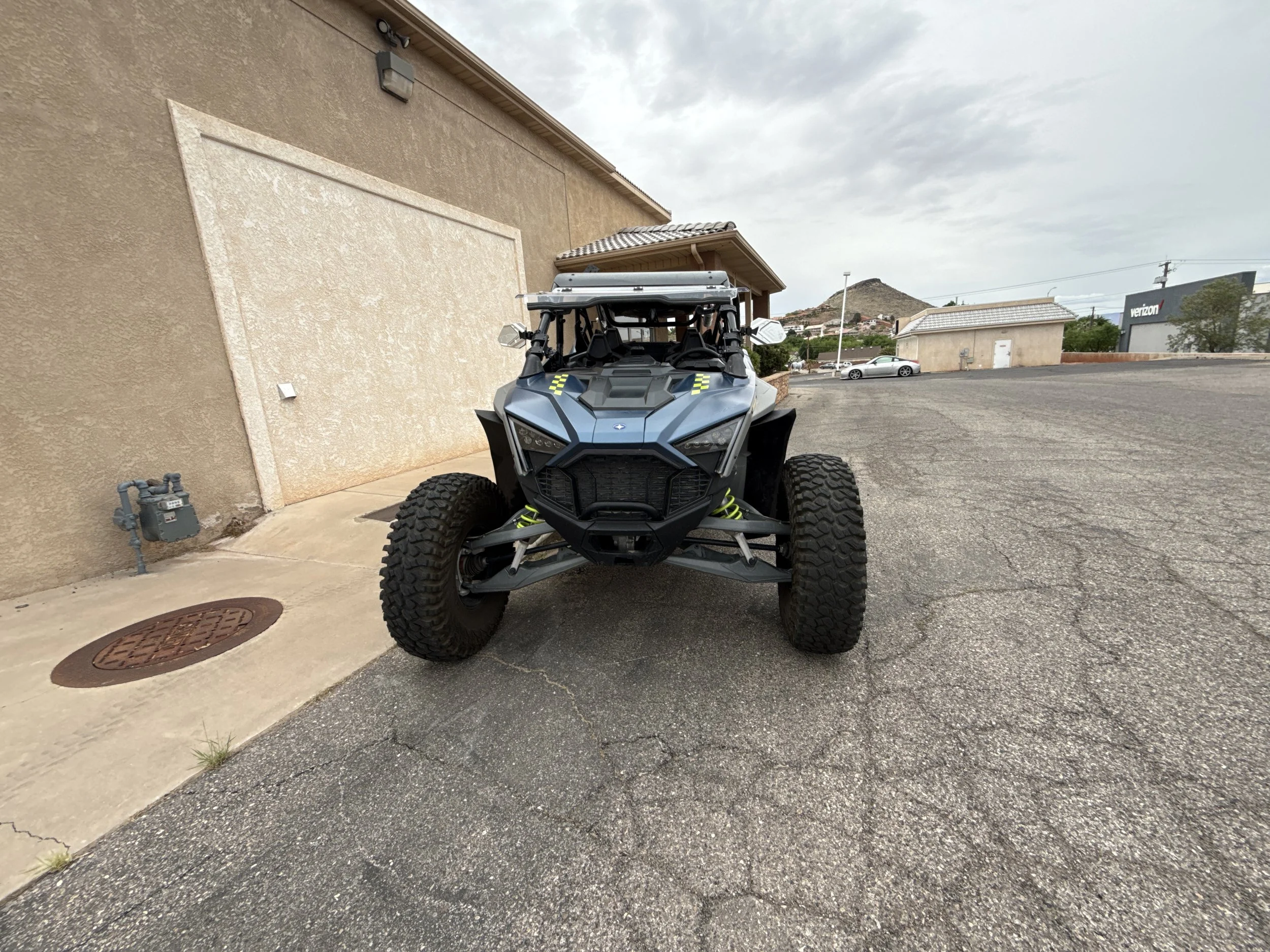 Close-up of a black off-road vehicle with a prominent grille and Suspension, parked in front of a business sign that reads Custom Sans Motor Sports, specializing in custom off-road vehicles.