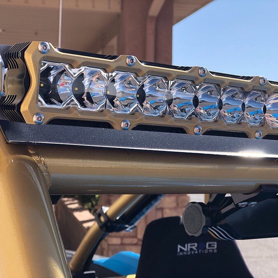 Close-up of a LED light bar mounted on a vehicle, with a stone and brick wall and blue sky in the background.