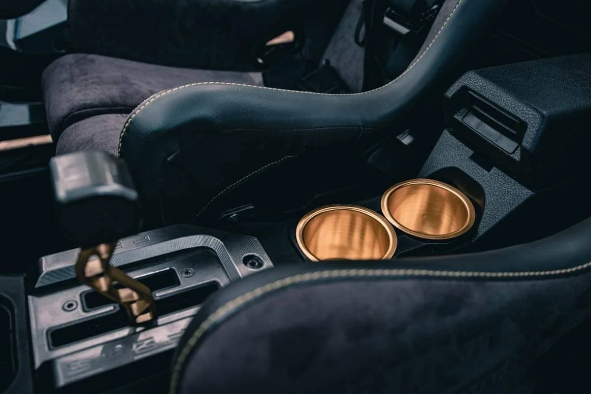 Inside a car showing the center console with two empty gold-colored cups and parts of the driver's seat.