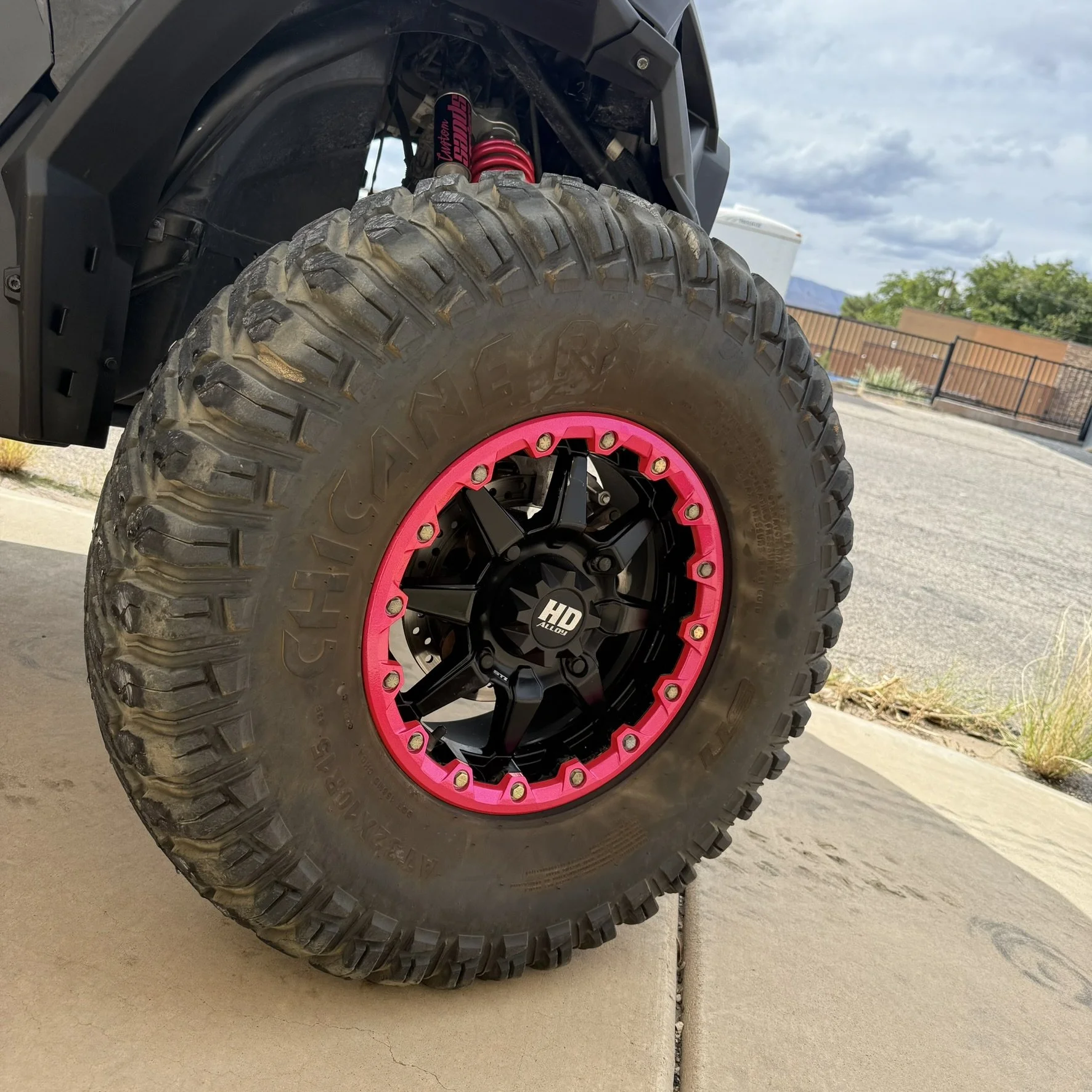 A man wearing a cowboy hat, sunglasses, and a red shirt sits on top of a black off-road vehicle with large tires. The vehicle has a sign that says 'BANDIT' on the roof and features gold accents and high-performance suspension.