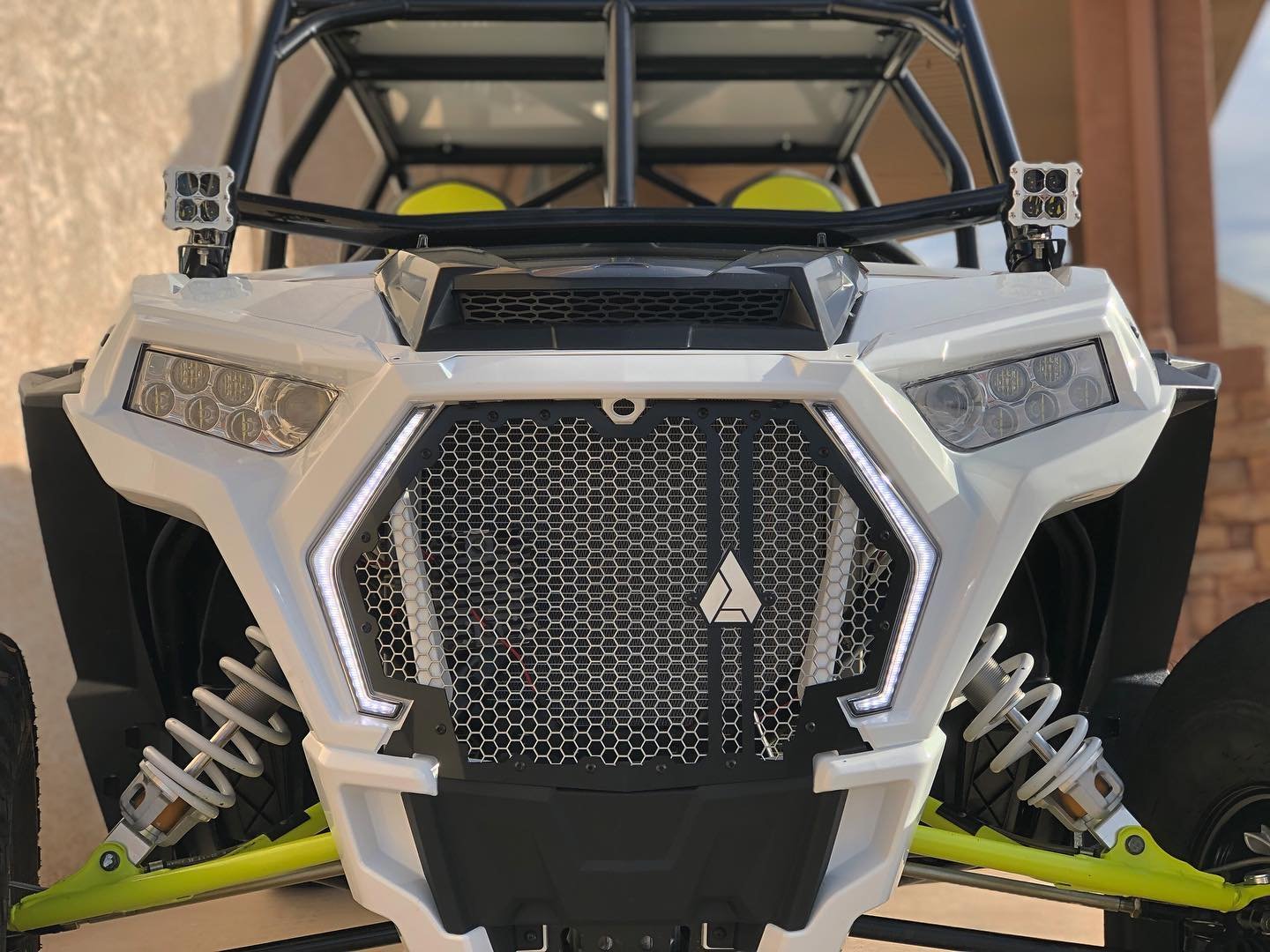 Front view of an off-road dune buggy with a white and black body, yellow suspension parts, and LED headlights, parked outdoors.