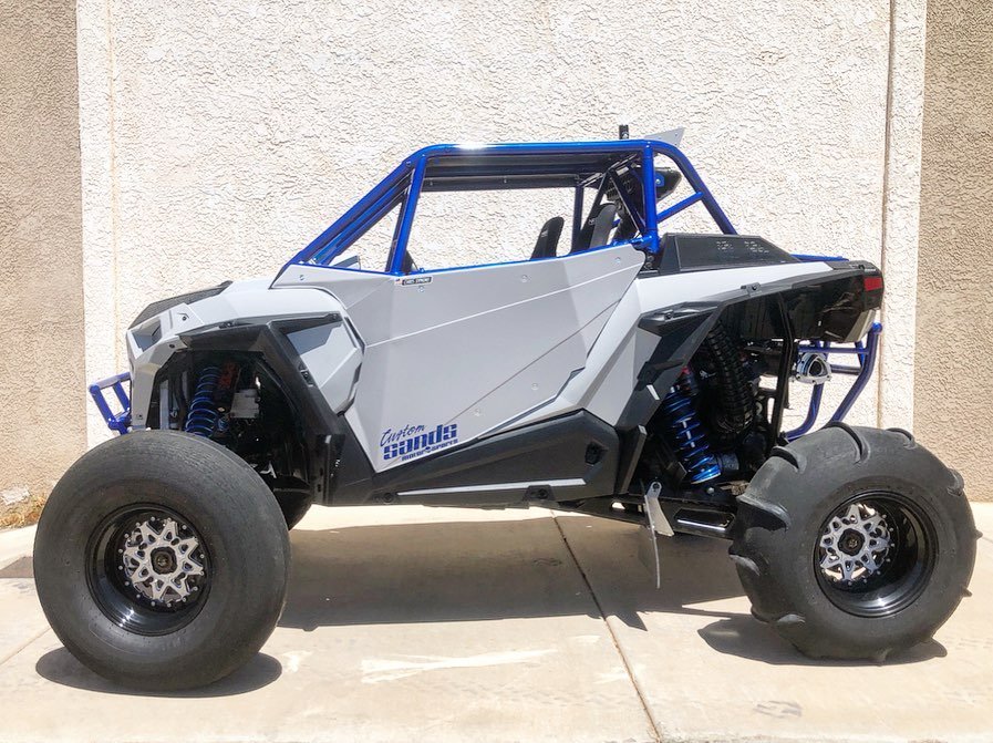 A custom-built off-road vehicle with large tires and a rugged, angular body design, parked on a concrete driveway.