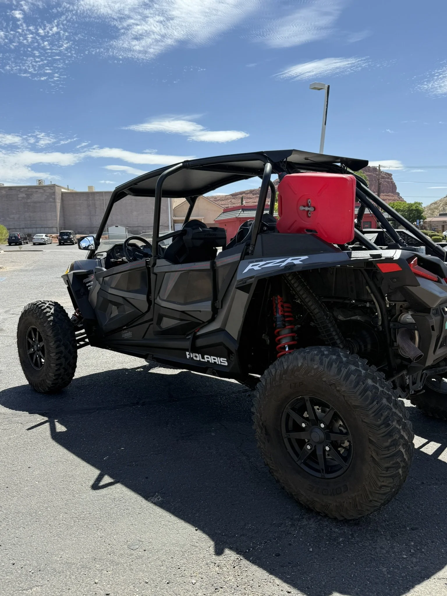 A black off-road dune buggy with large tires, roll cage, and visible suspension system parked on a concrete sidewalk next to a beige wall.