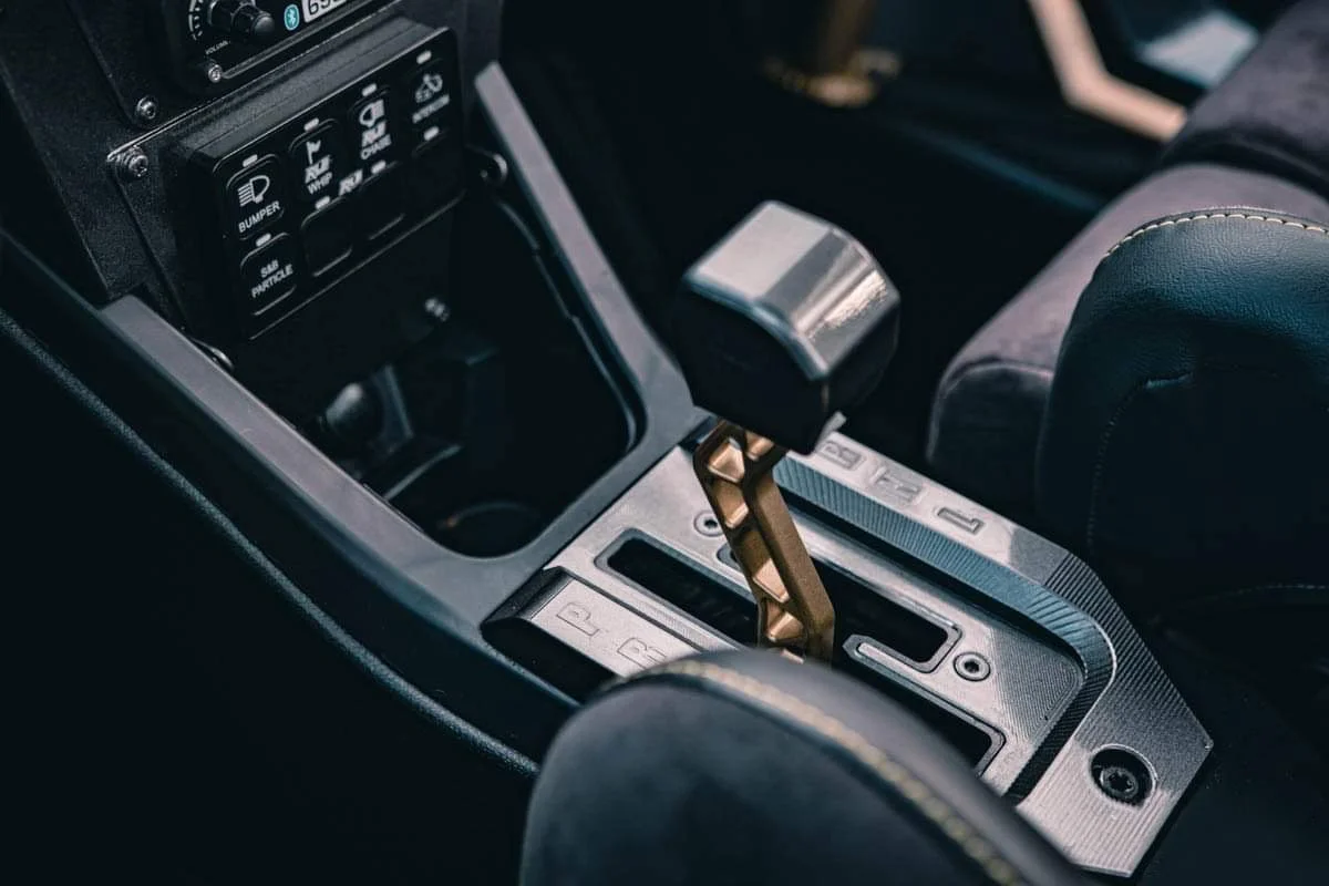 Close-up of a luxury car gear shift lever in the center console, surrounded by various driving mode options and electronic controls.