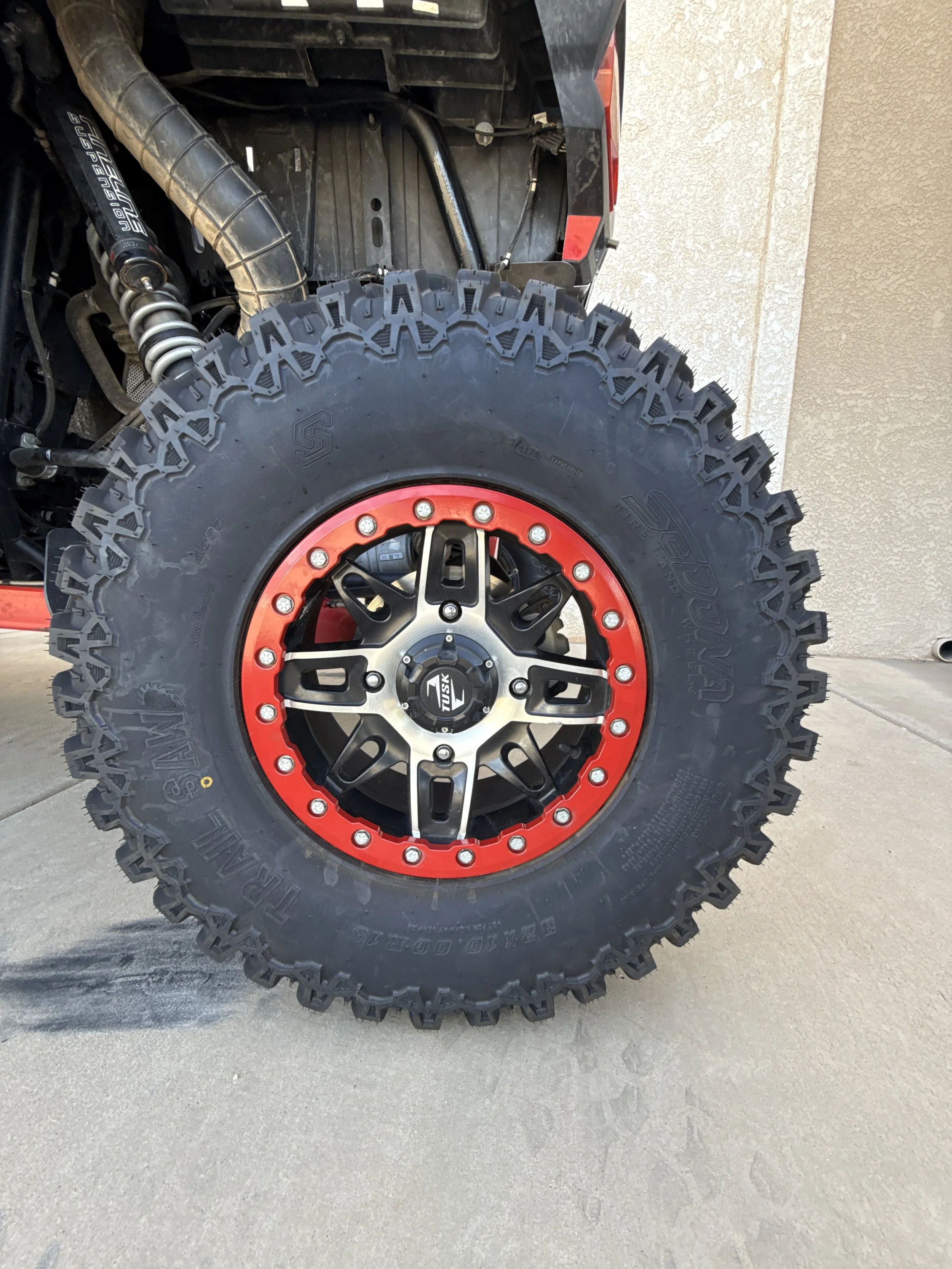A black off-road dune buggy with large tires, roll cage, and visible suspension system parked on a concrete sidewalk next to a beige wall.