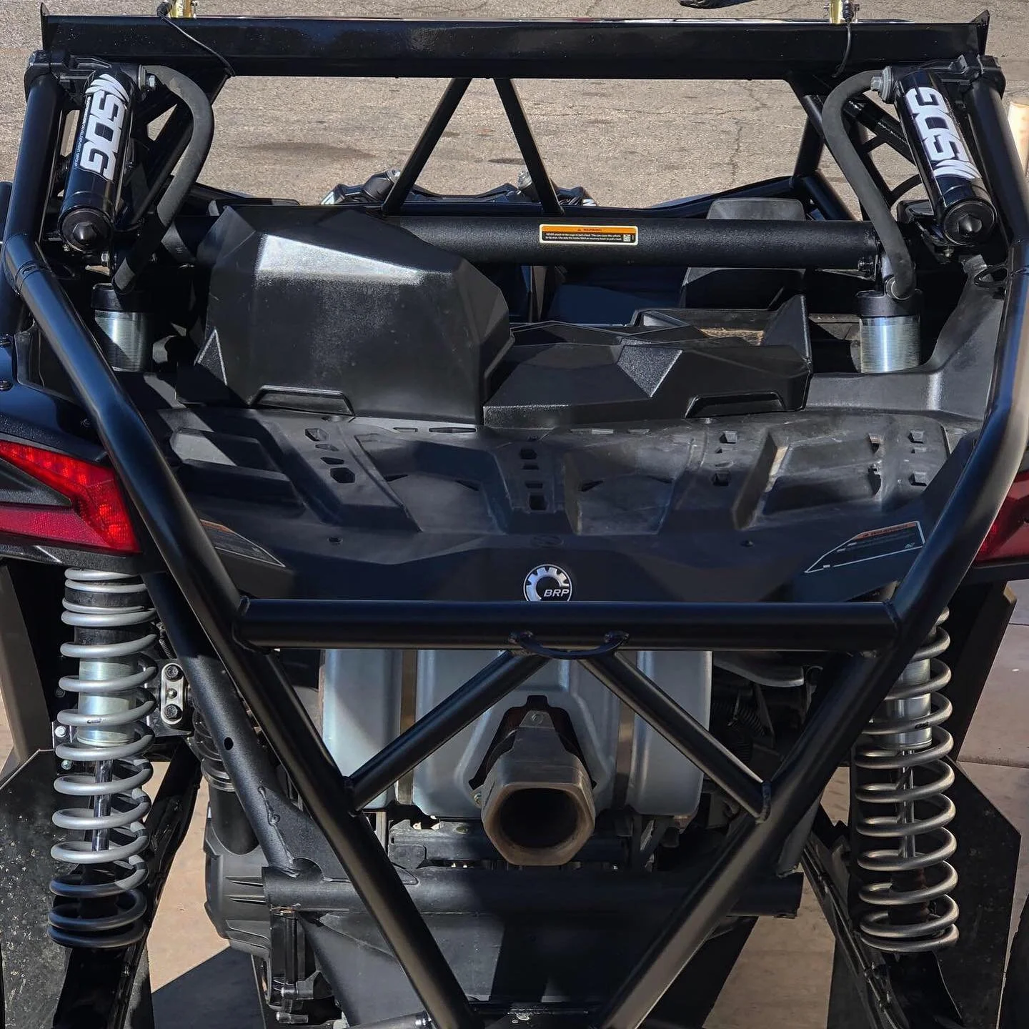 Close-up of a vehicle's rear engine compartment revealing a black BRP logo, shock absorbers, and mechanical components.