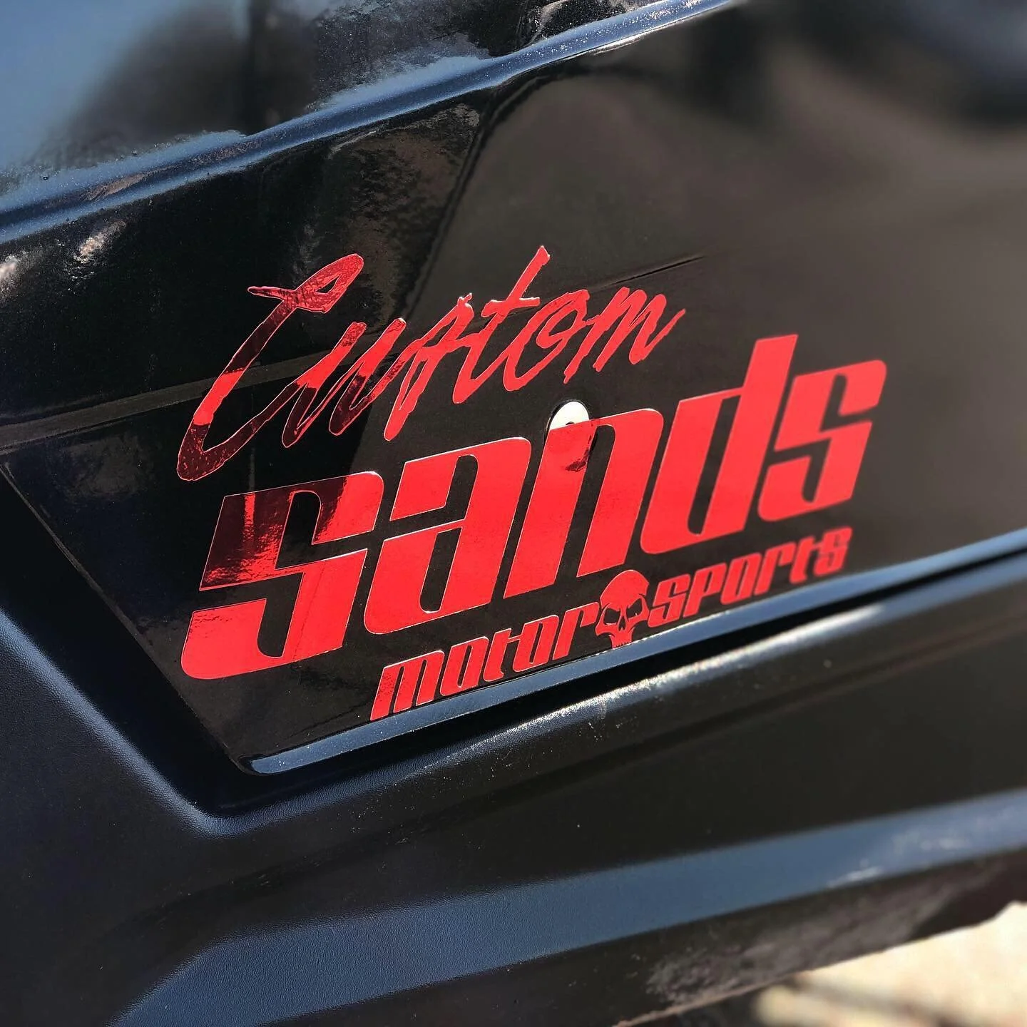 Close-up of a black surface with red and white decal reading 'Custom Shadows motorsports' with a skull logo.