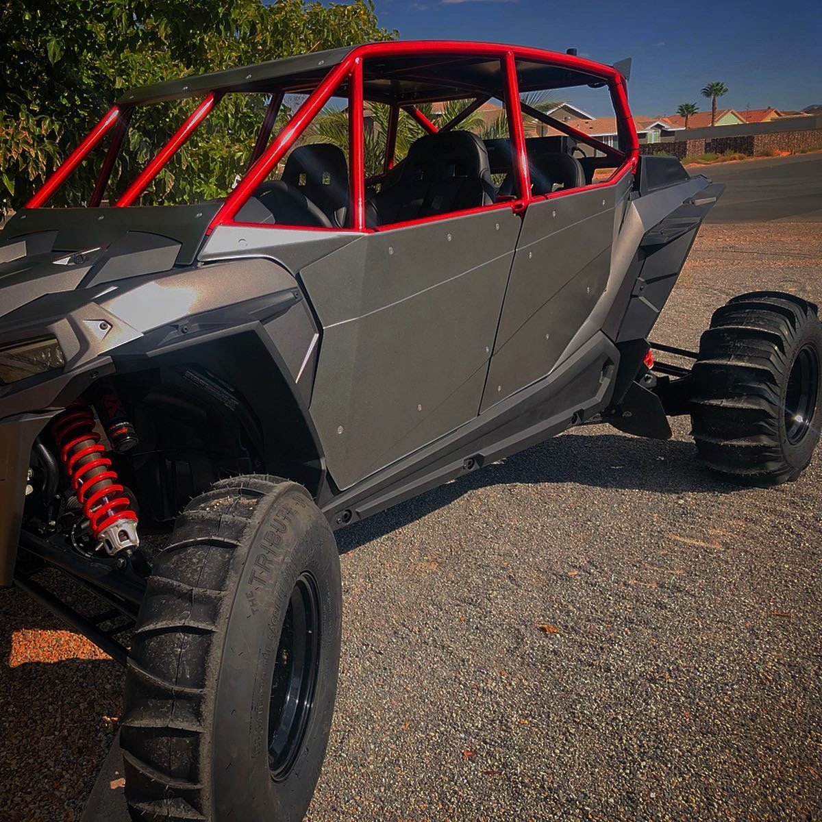 A custom off-road vehicle with large tires, red suspension coil springs, and a red roll cage, parked on a paved road.