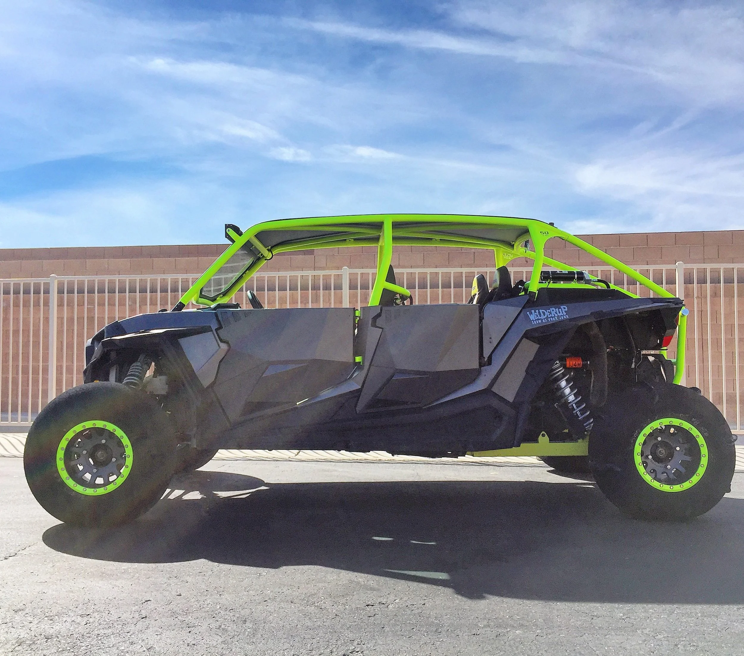 Off-road electric dune buggy with black body and lime green roll cage parked on concrete surface under blue sky.