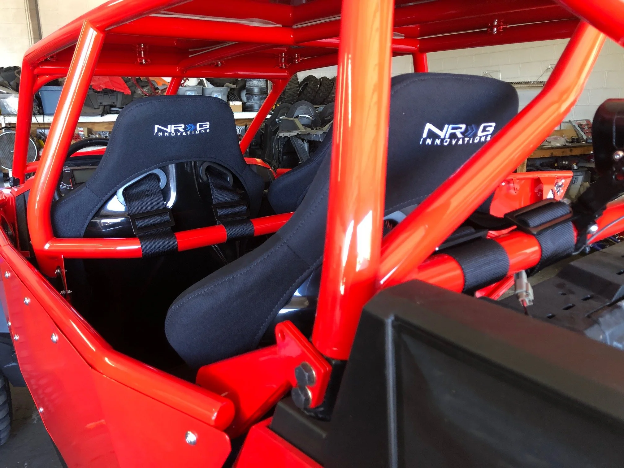 Interior of a red race car with black NR G Innovations racing seats and safety harnesses.