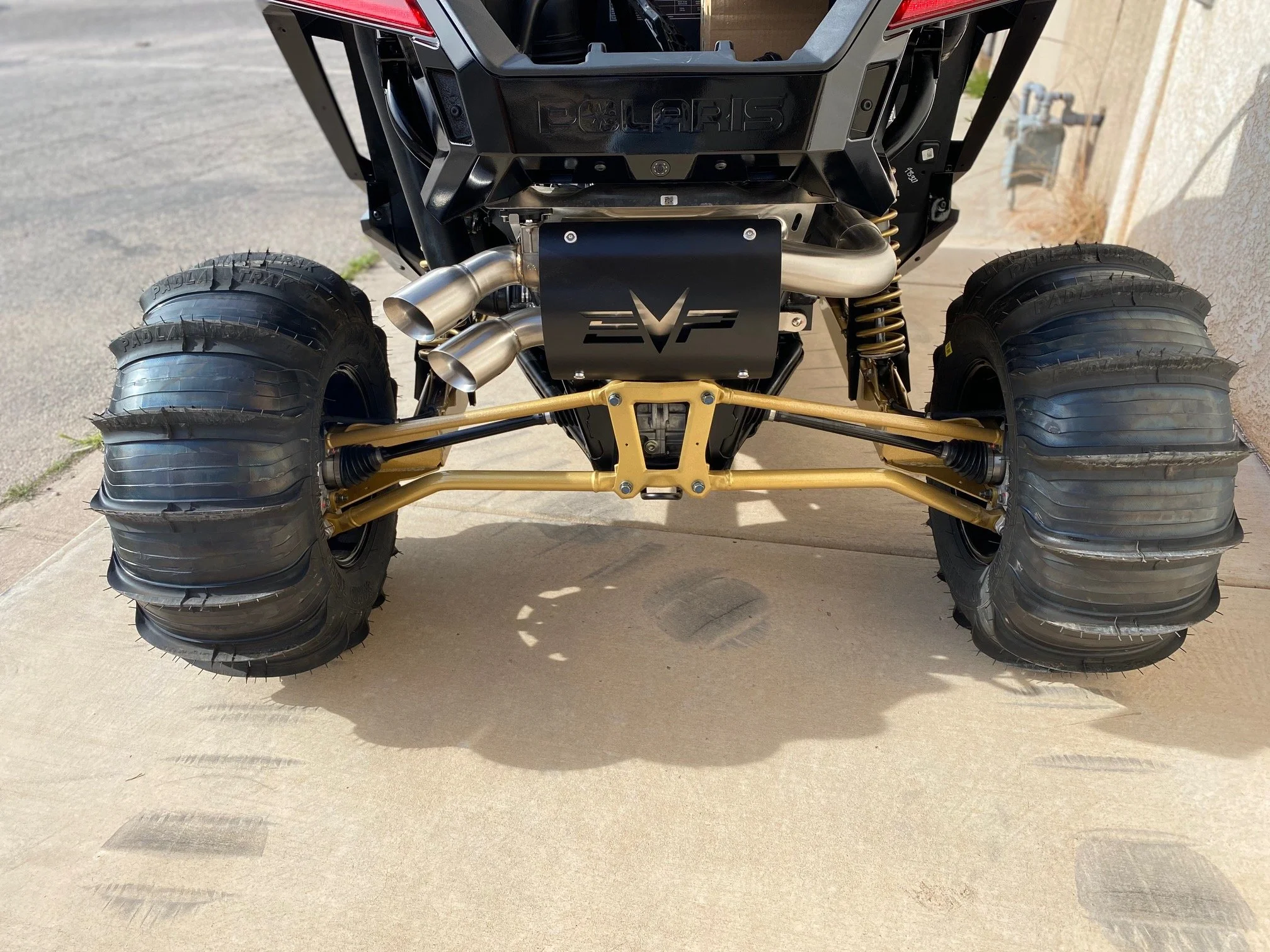 A close-up view of the front suspension and wheels of a Polaris EV off-road vehicle, featuring large knobby tires, yellow suspension arms, and a black 4x4 bumper.