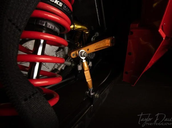 Close-up of a car's suspension system, showing a red coil spring, a gold-colored shock absorber, and a black suspension arm.
