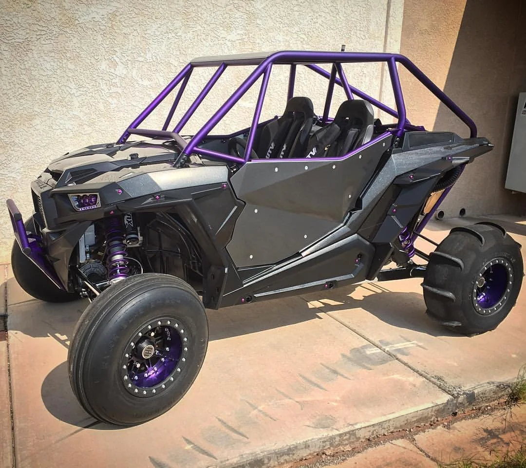 A custom-built off-road vehicle with a black and purple frame, four large tires, and two black racing seats.
