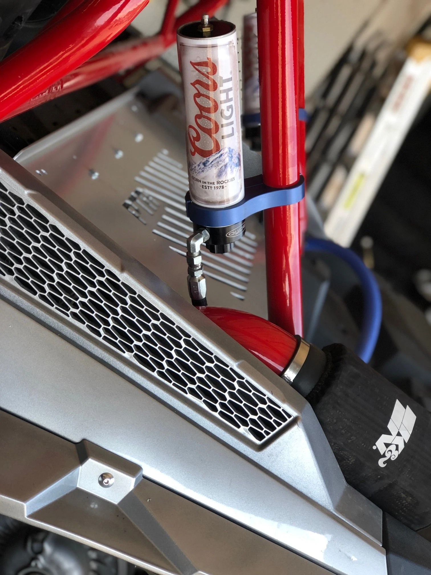 Close-up of a 3D printer with a Coca-Cola Light can attached underneath a red frame, showing part of the printer's structure and components.