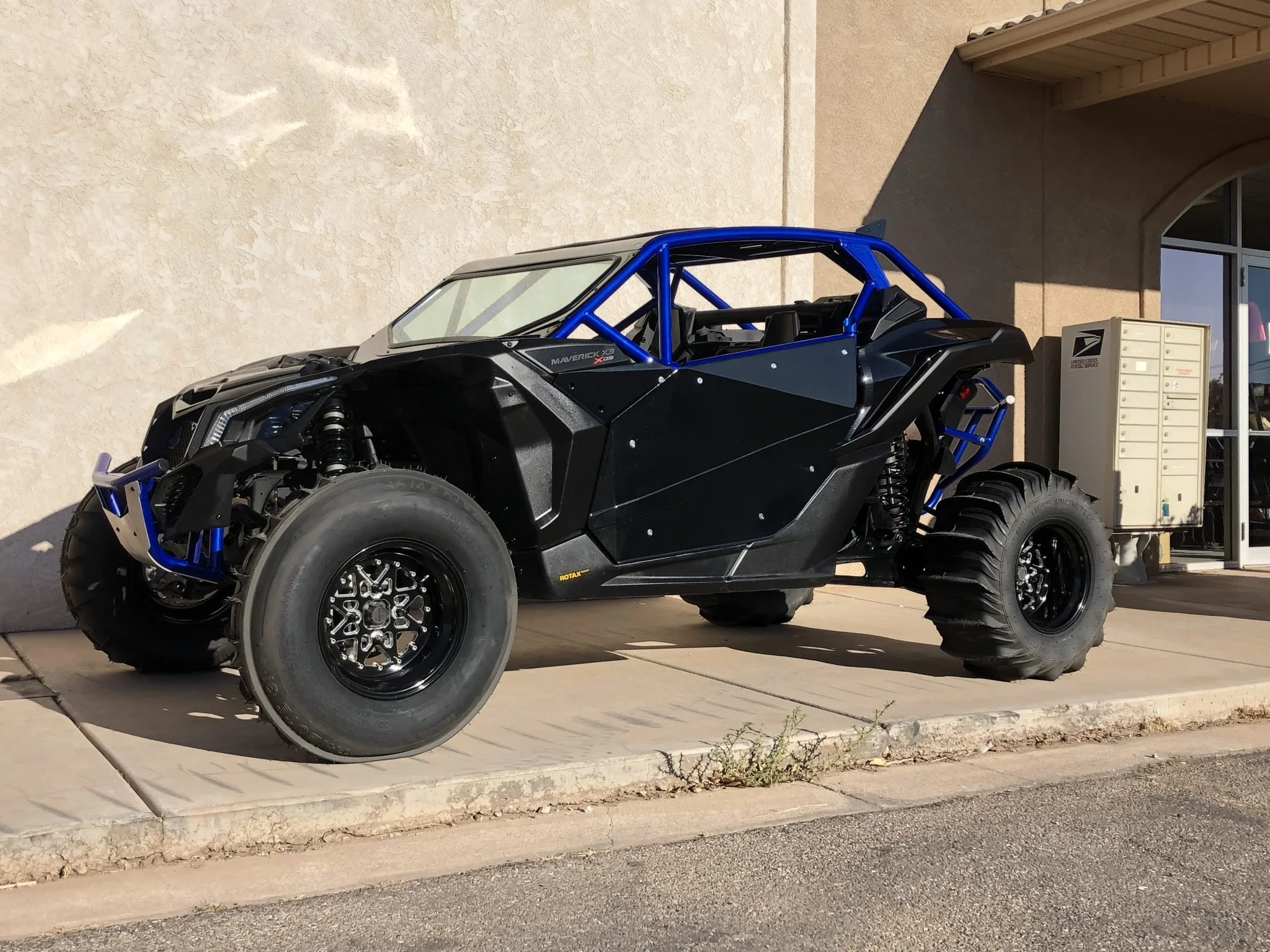 Off-road electric dune buggy with black and blue frame, parked outside a building.