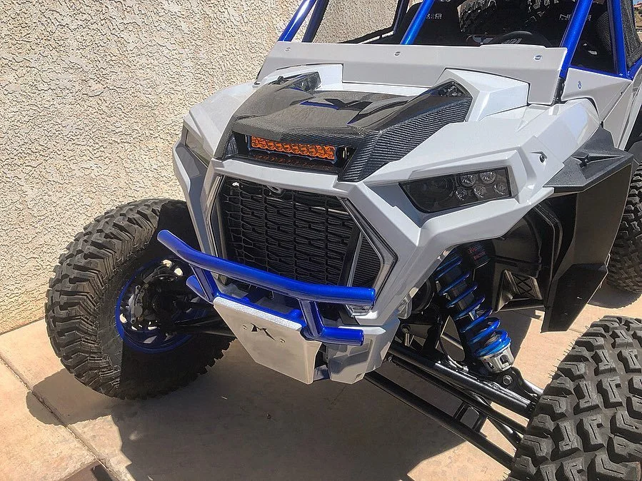 A custom off-road vehicle with large tires, a white body, blue accents, and a protective bumper.