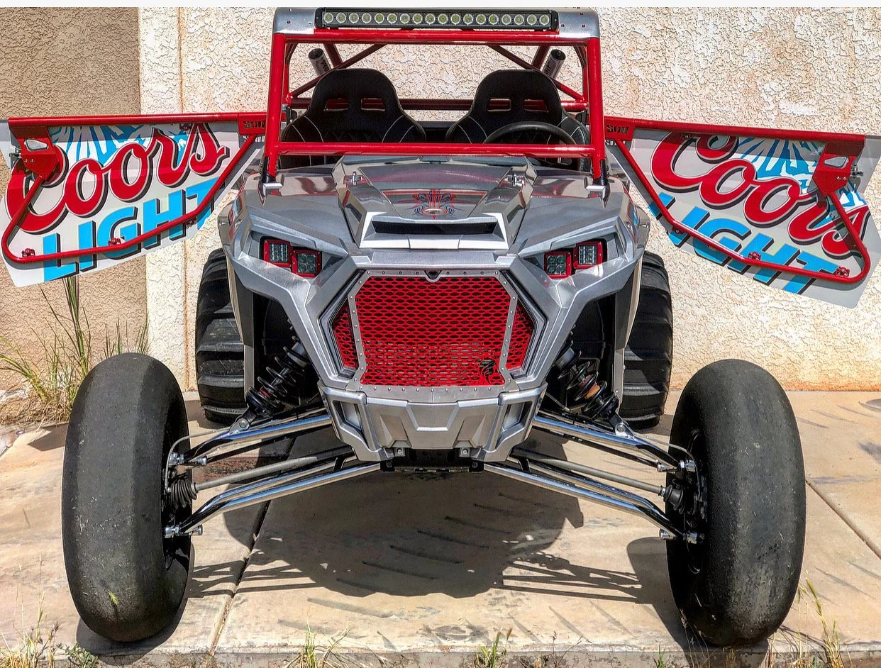 Front view of a small off-road racing vehicle with large tires, a metal frame, and Coors Light sponsorship decals on the wing panels.