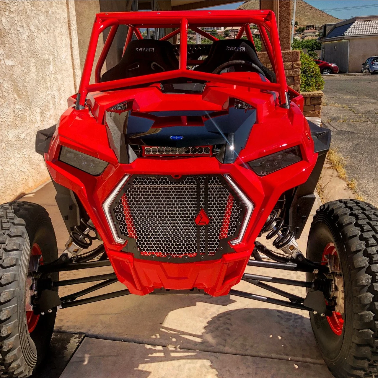 Front view of a red off-road vehicle with a black grill, mounted lights, large tires, and a roll cage.