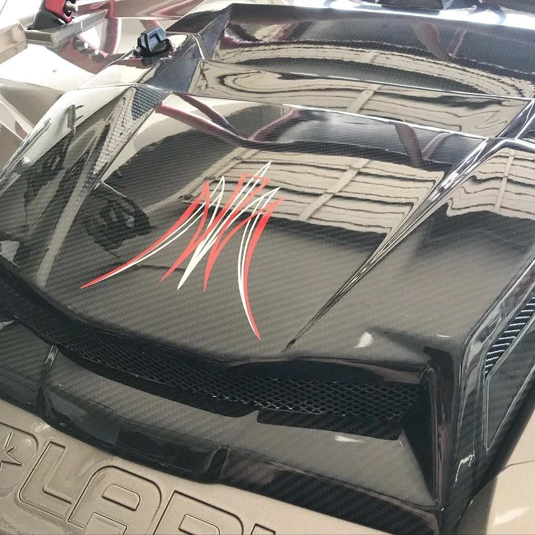 Close-up of a black sports car with carbon fiber accents and red and white pinstripe decal on the hood.