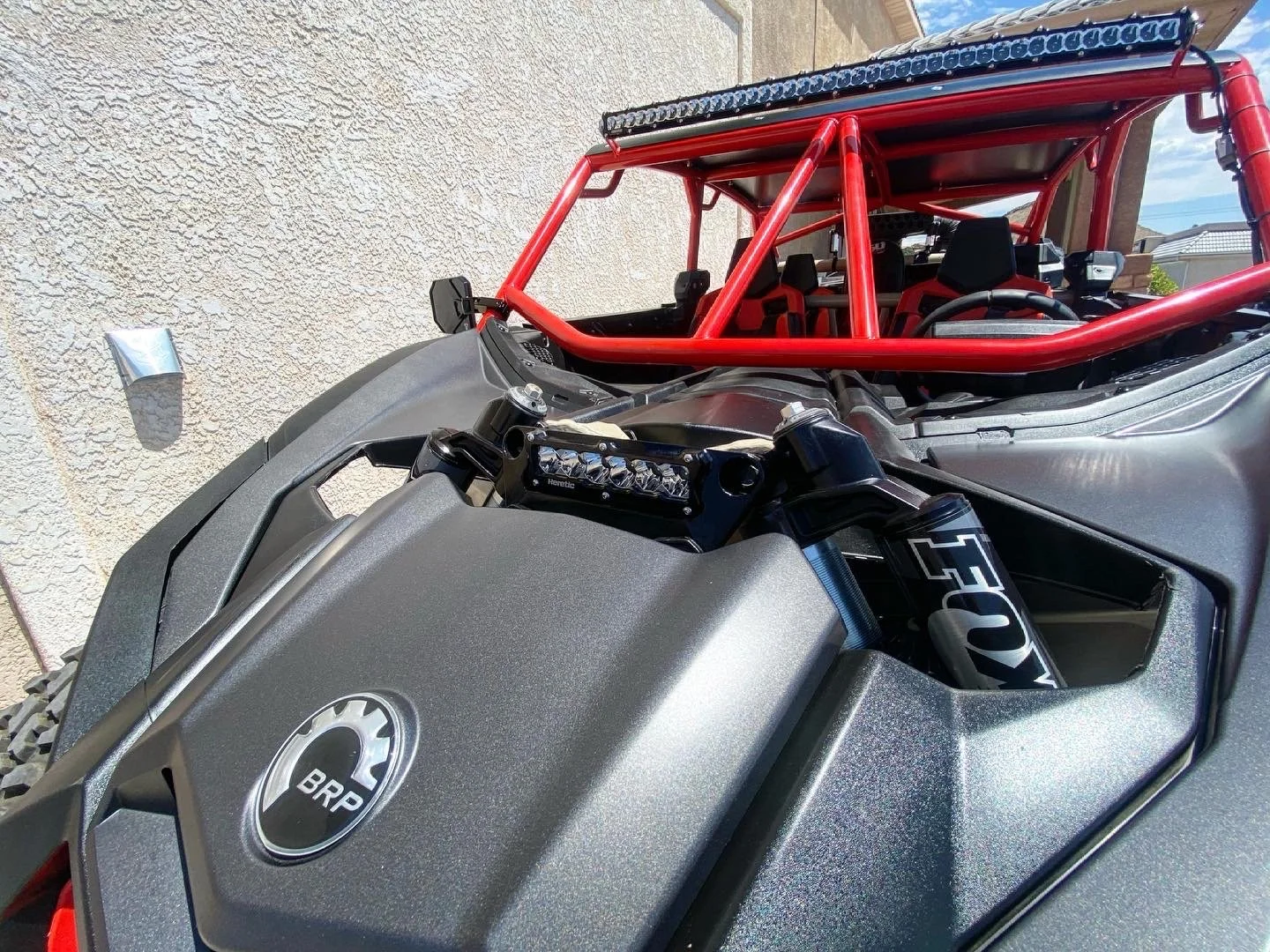 A close-up view of a customized off-road vehicle with a BRP logo on the hood, featuring a grey body, red roll cage, and a black suspension system with Fox shocks.