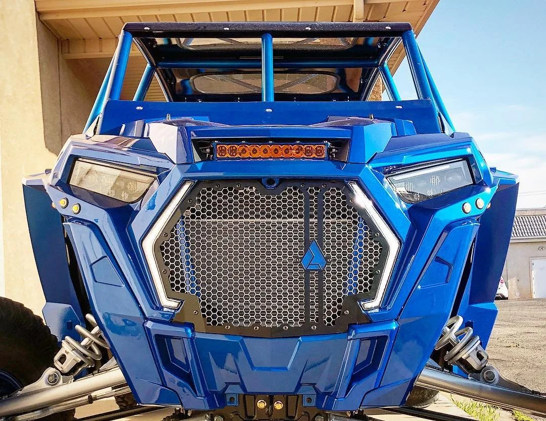 Blue off-road utility vehicle with angular design, large grille, and LED lights, parked outdoors.