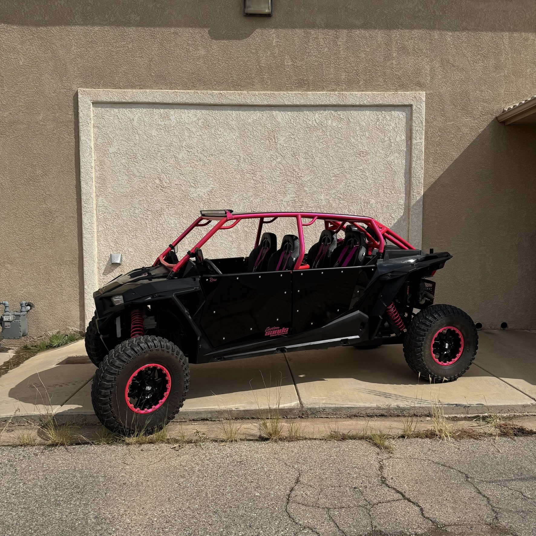Off-road vehicle with large tires, suspension, and a custom front grille, parked on a dirt path surrounded by stone walls and trees, with a sign reading 'BANDIT' on top.